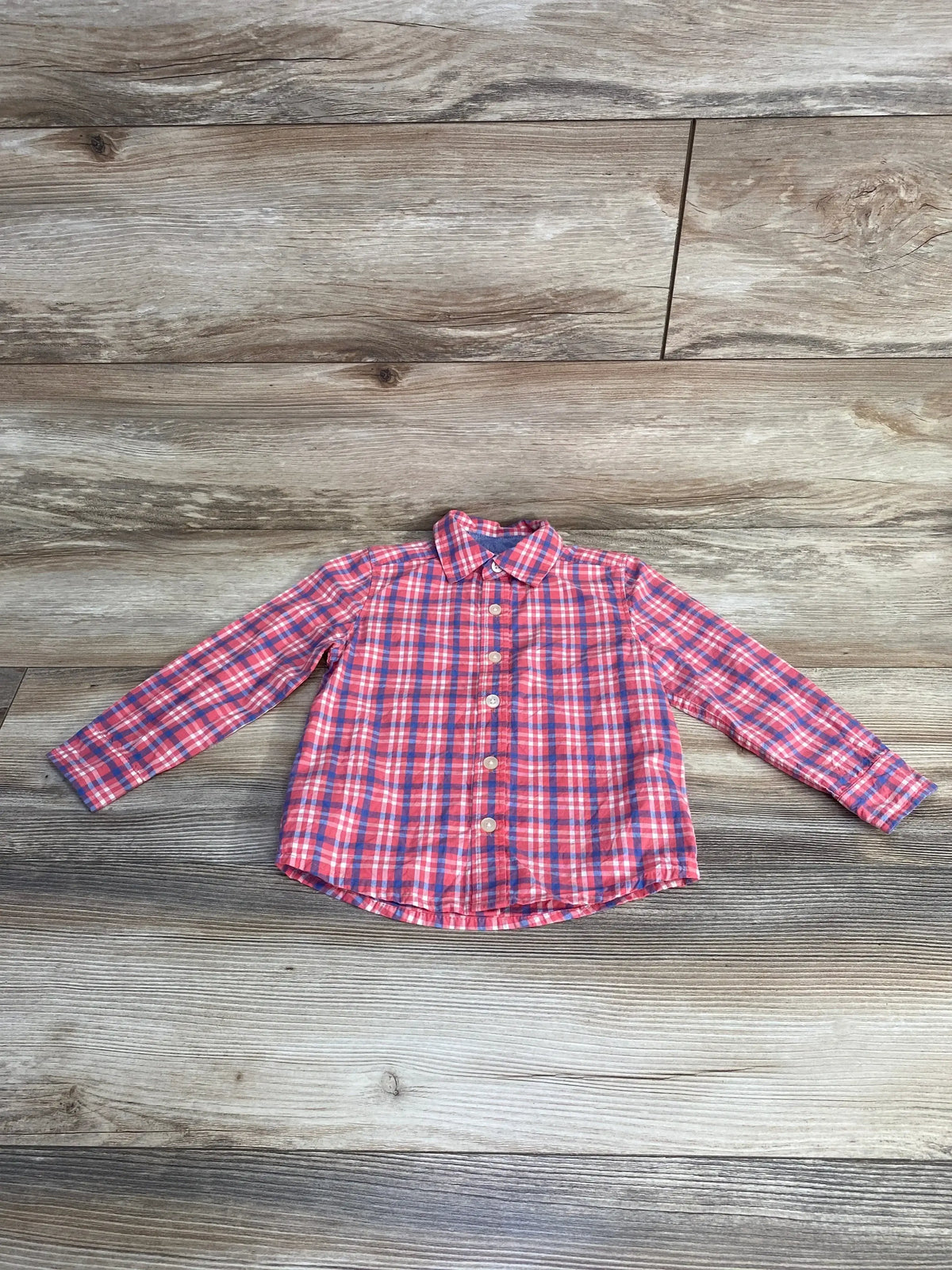 Front view of pink OshKosh plaid button-up shirt size 3T with long sleeves and full button front on wood background