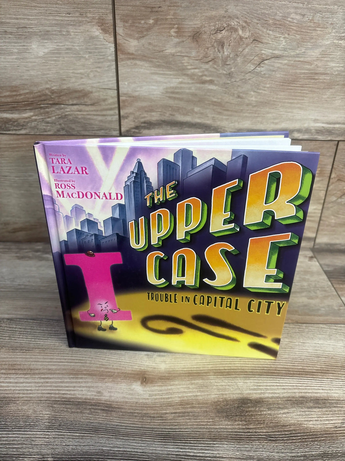 Front cover of The Upper Case: Trouble in Capital City hardcover book with colorful uppercase-letter artwork against a city skyline