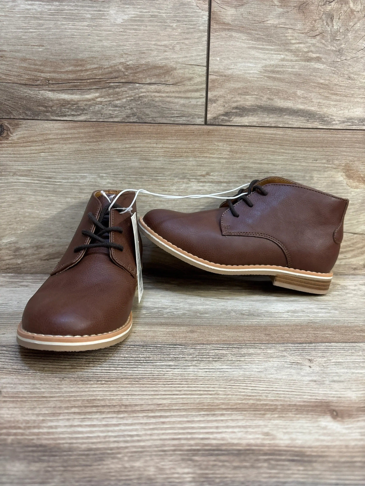Brown leather kids lace-up boots with rubber soles on wood floor