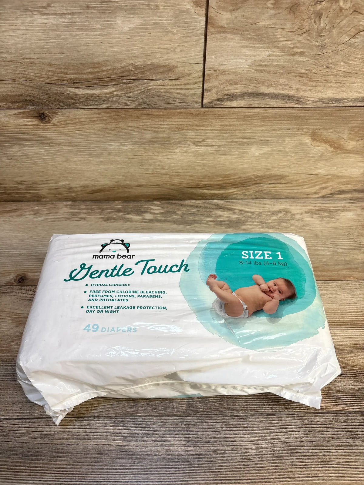 Front view of Mama Bear Gentle Touch Size 1 diaper pack showcasing baby photo, Size 1 (8-14 lbs) label and 49 diapers text on wood background