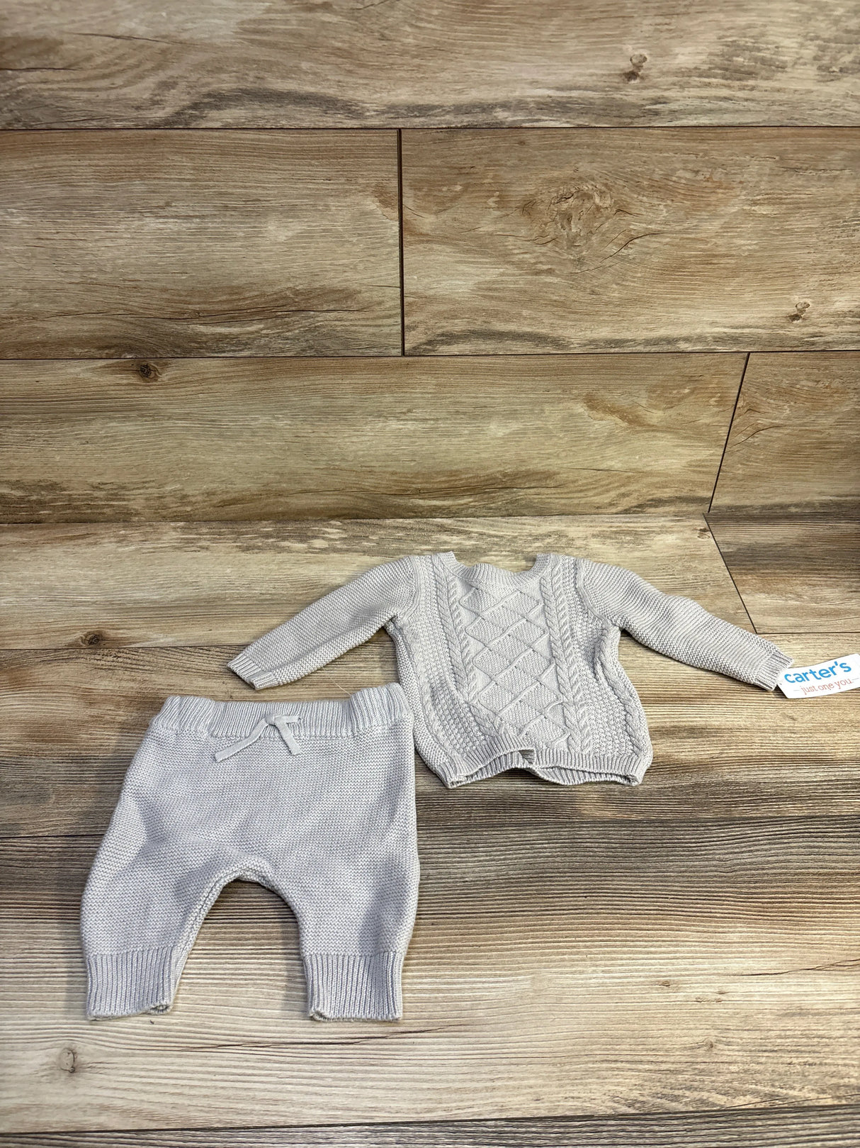 Flat lay of grey 2-piece baby knit sweater and pants set showcasing cable-knit sweater and ribbed cuffs on wood background