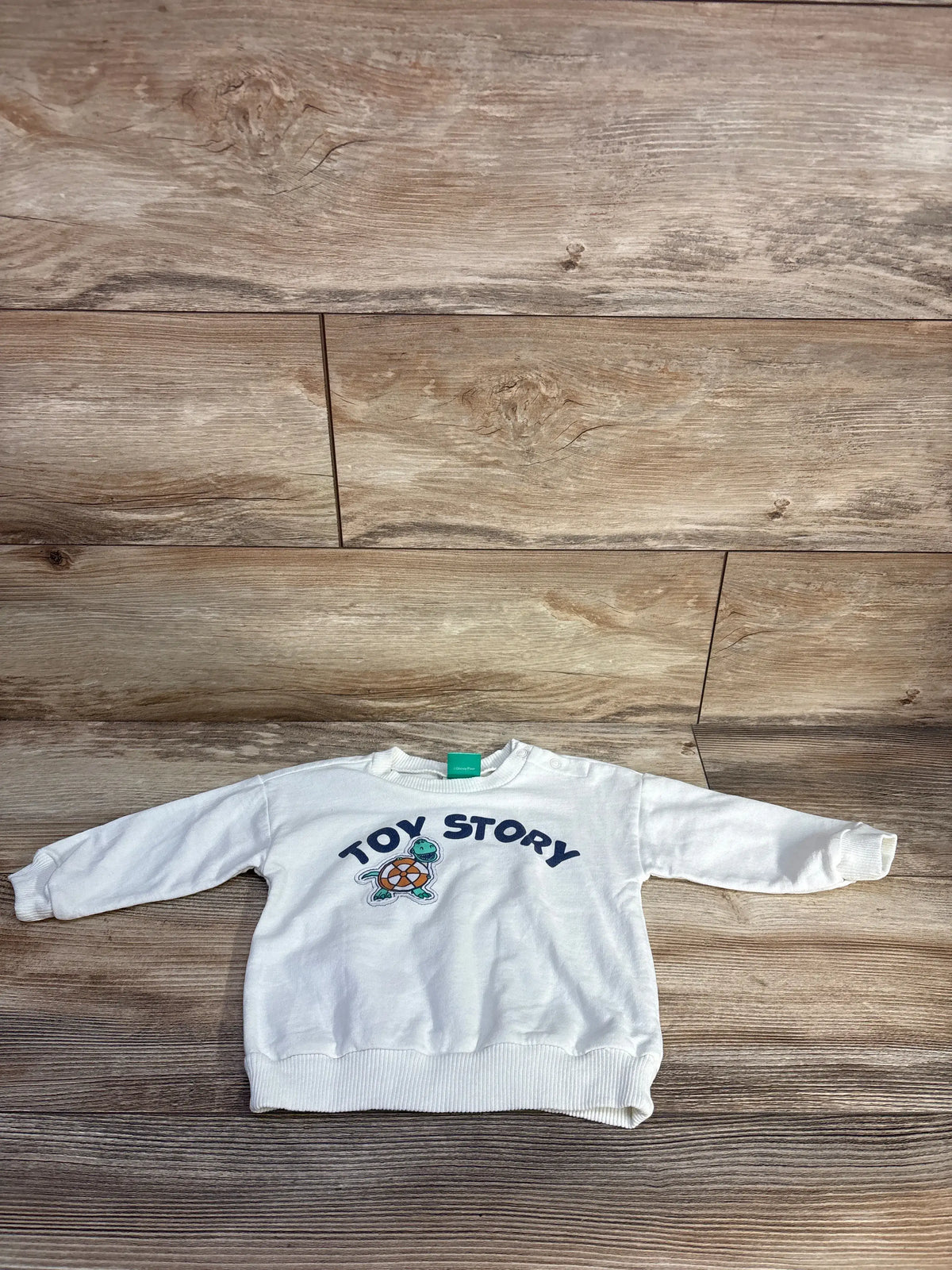 Front view of Disney Baby Toy Story sweatshirt showcasing ivory fabric, character graphic, and ribbed trim on a wood floor