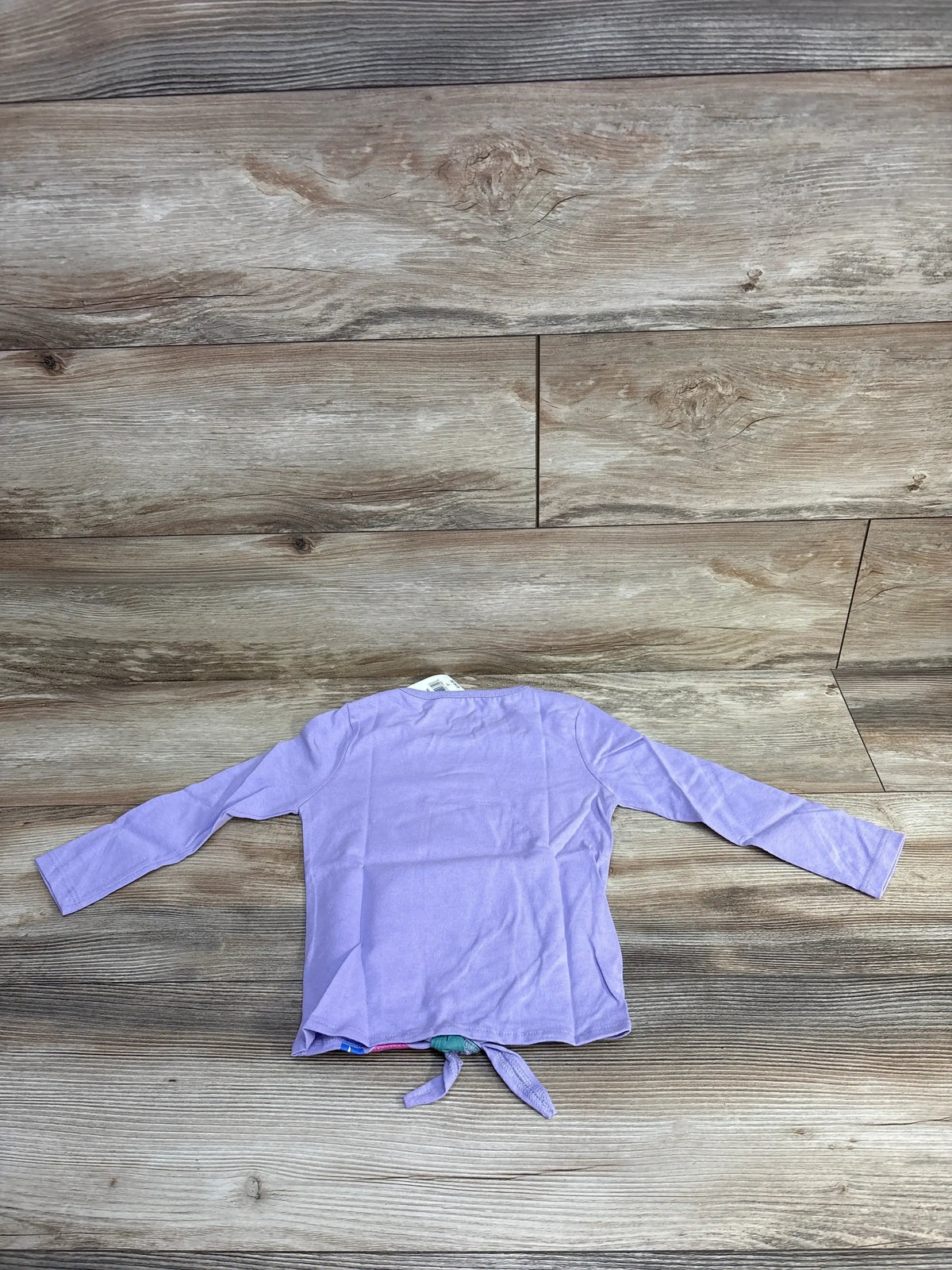 Lilac long-sleeve toddler shirt laid flat on rustic wood floor with tied knot at hem