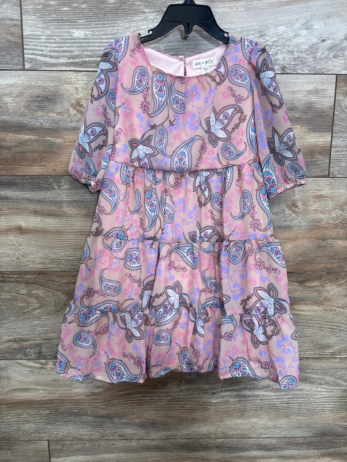 Front view of kids’ paisley tiered dress in dusty rose showcasing three-tier ruffle skirt and puff sleeves on wood floor background
