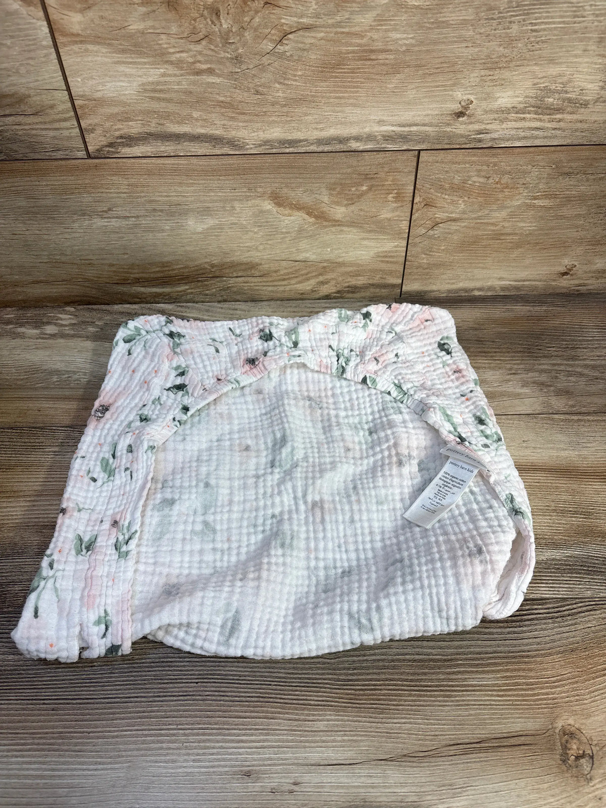 Top view of Pottery Barn Kids organic cotton changing pad cover showing elastic edges and floral trim on a wood floor