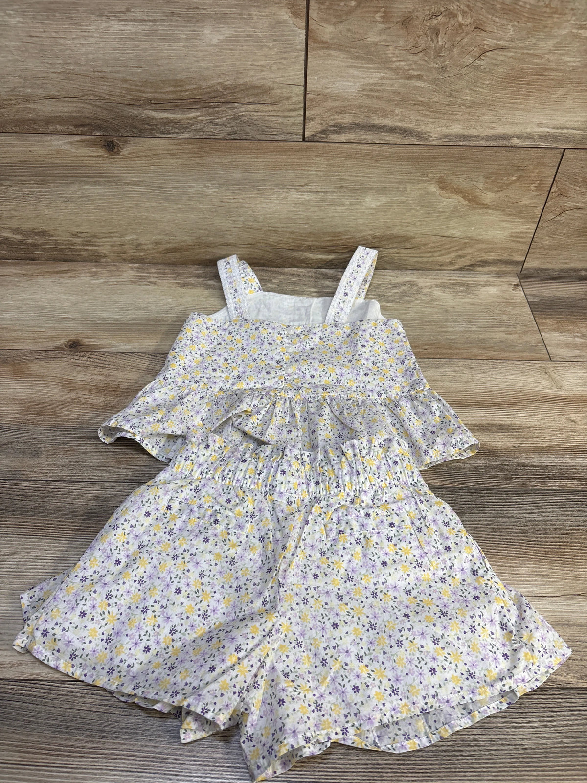 Front view of a white ditsy floral outfit with thin straps and a tiered lower section on a wood-patterned floor
