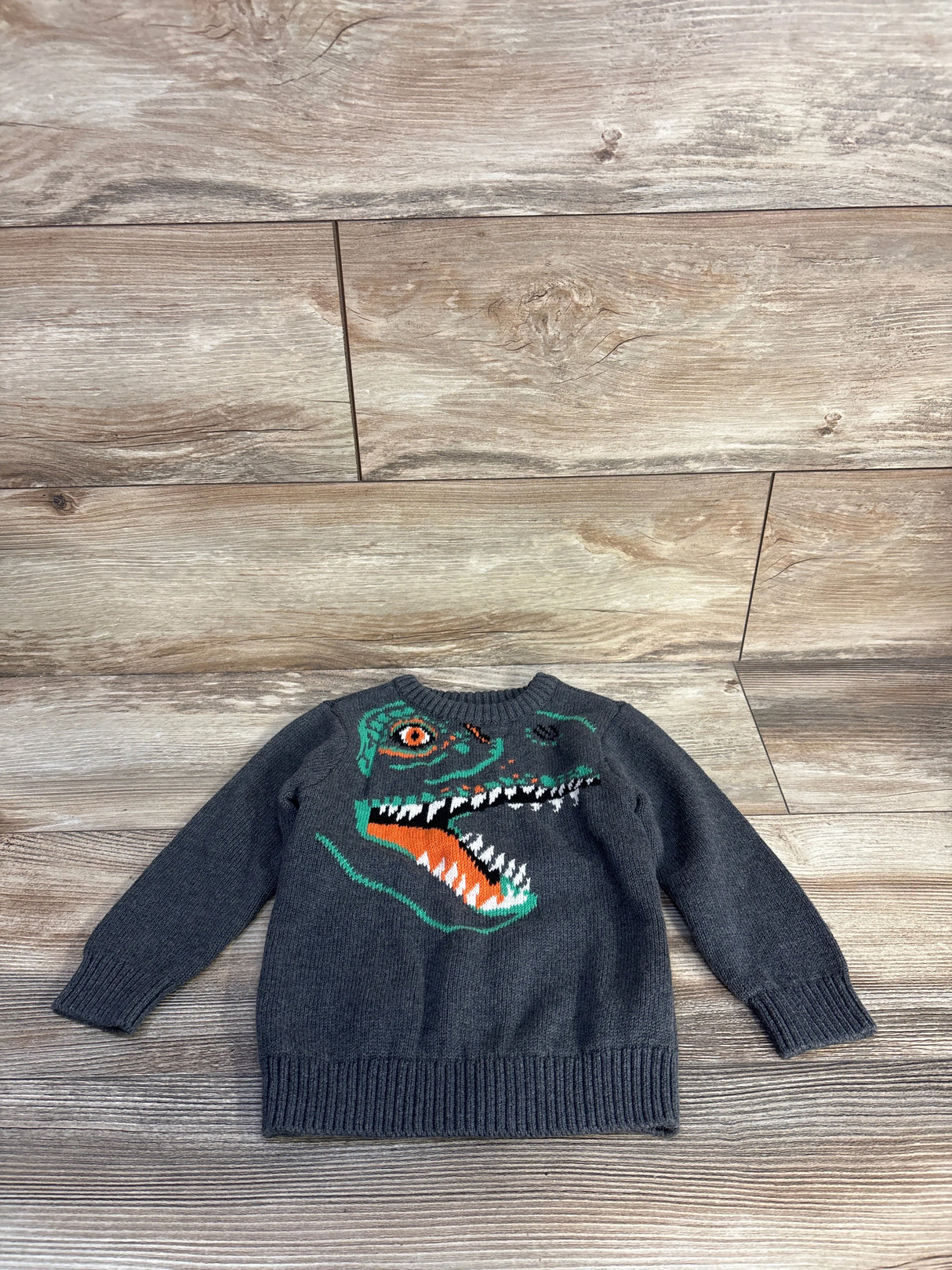 Flat lay grey Old Navy crewneck sweater 2T with green and orange dinosaur head graphic and ribbed cuffs on wood floor