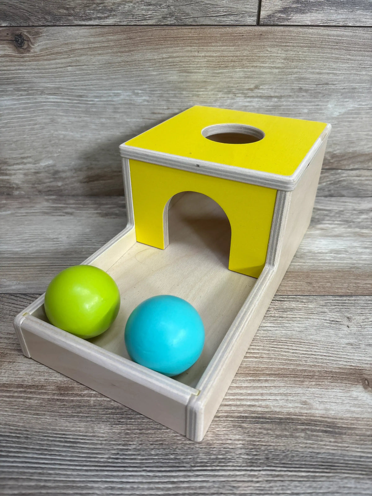 Wooden Montessori toy with yellow top, two colorful balls, and natural finish