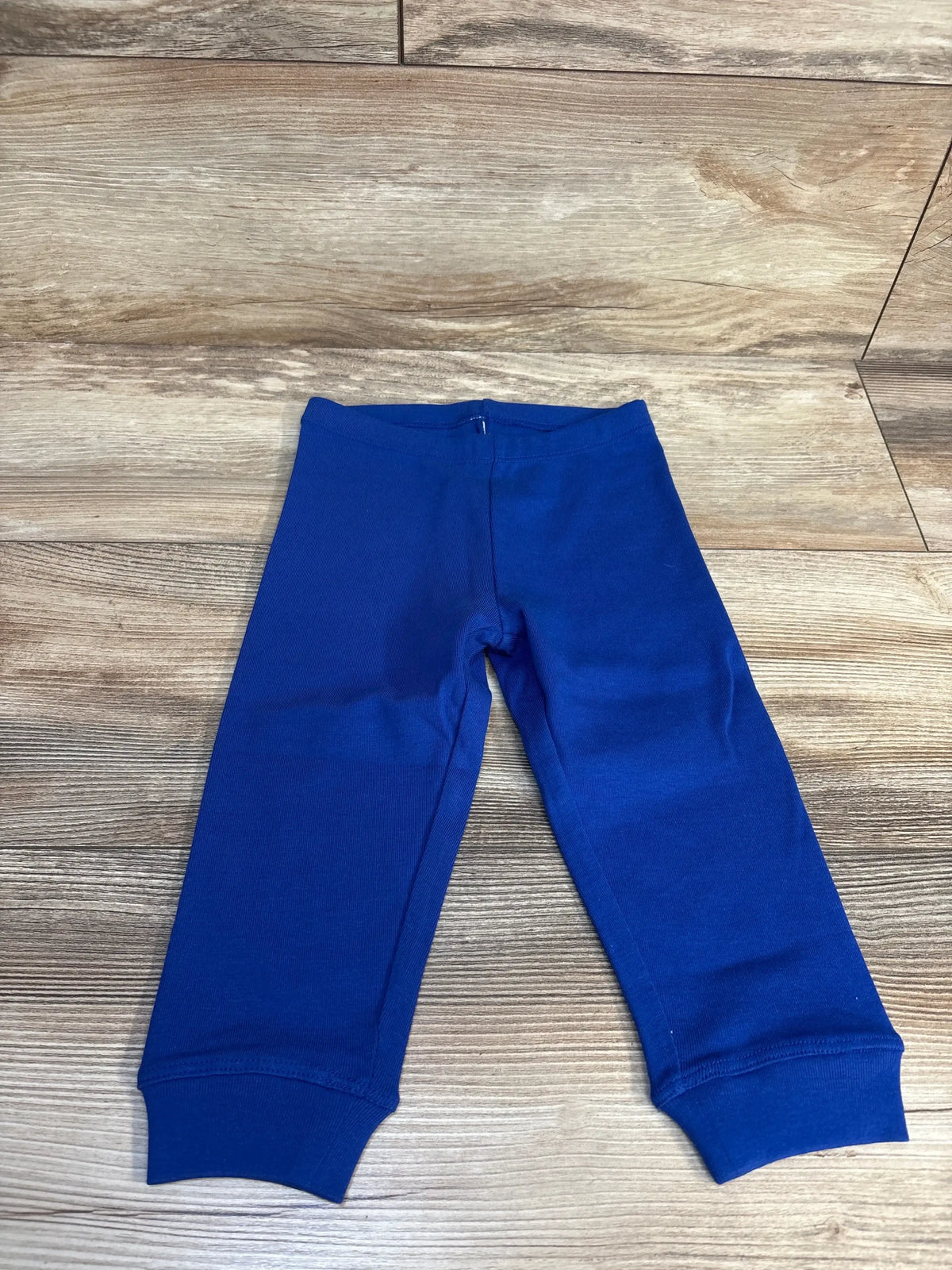 Top-down view of blue toddler leggings, size 12-18 months, showing elastic waistband and cuffed ankles on wood floor