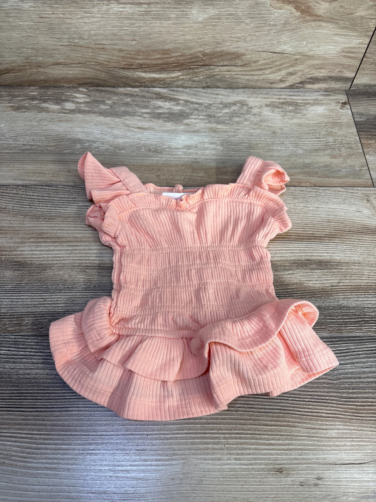 Flat lay of peach smocked tank top size 18M with smocked bodice, ruffle hem and flutter sleeves on wood background