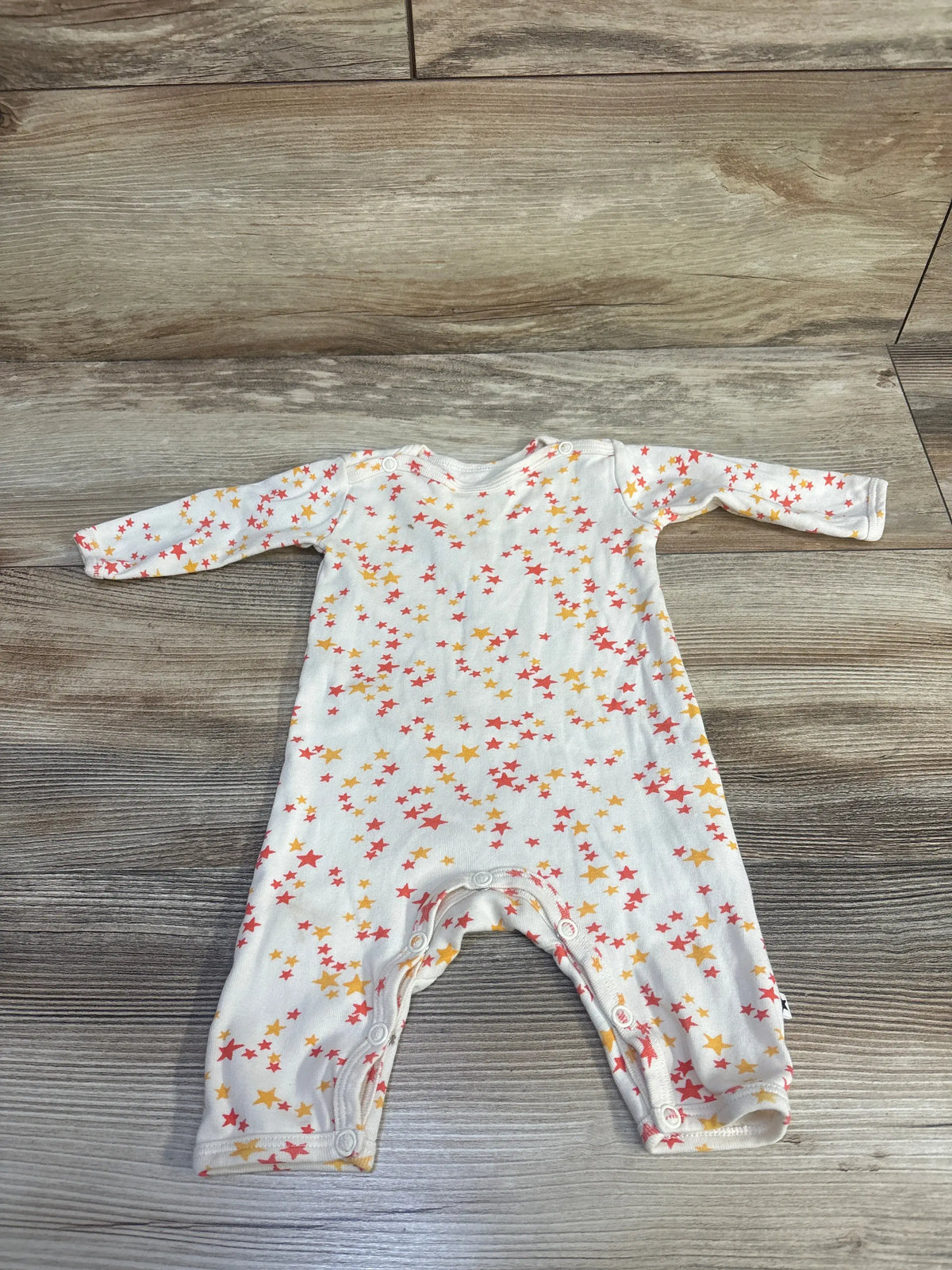 Front view of Molo Fenez newborn coverall in cream showcasing star print, long sleeves, and front snaps on a wood floor