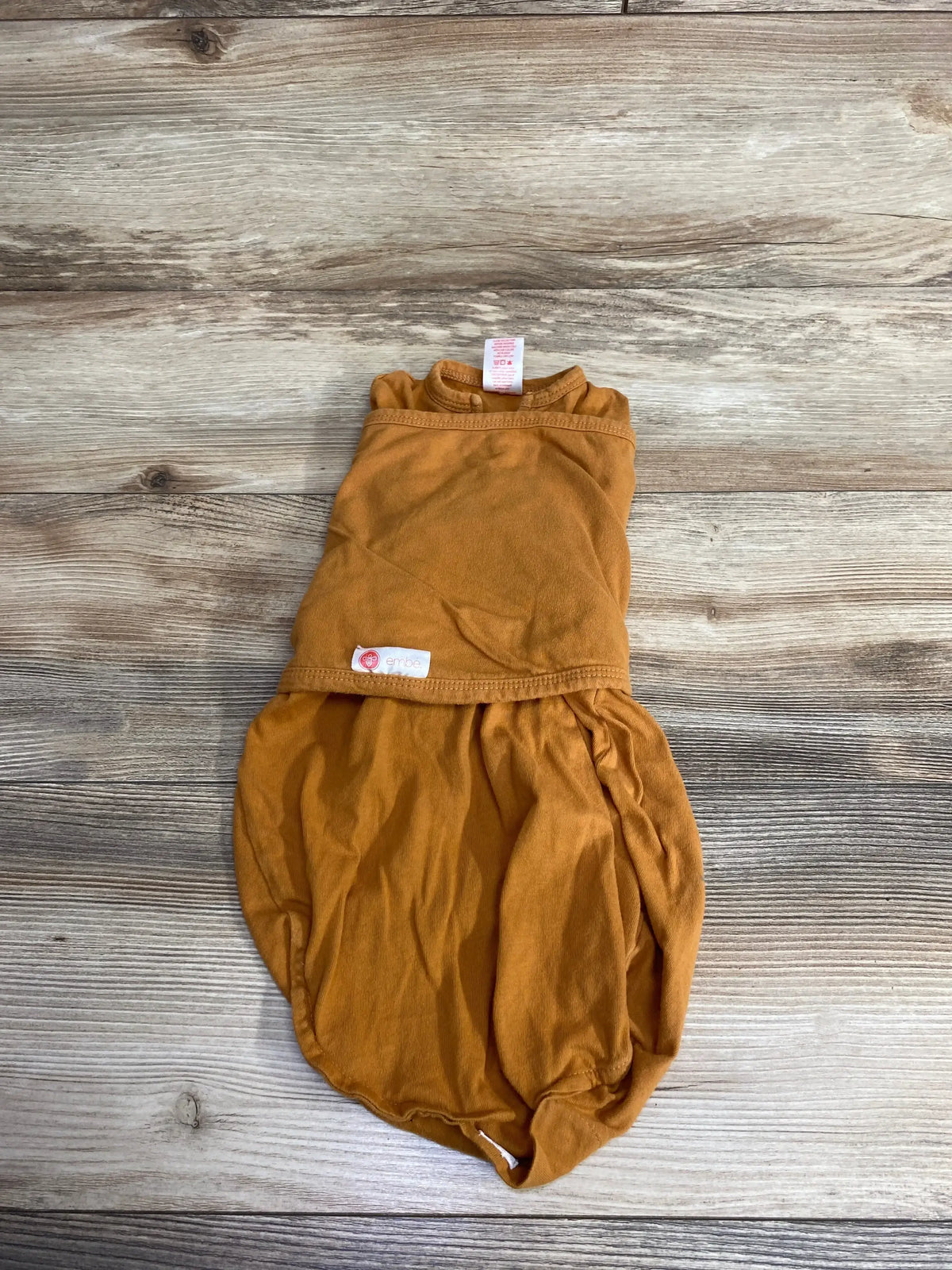 Embe brand rust-colored baby swaddle blanket on wooden floor background