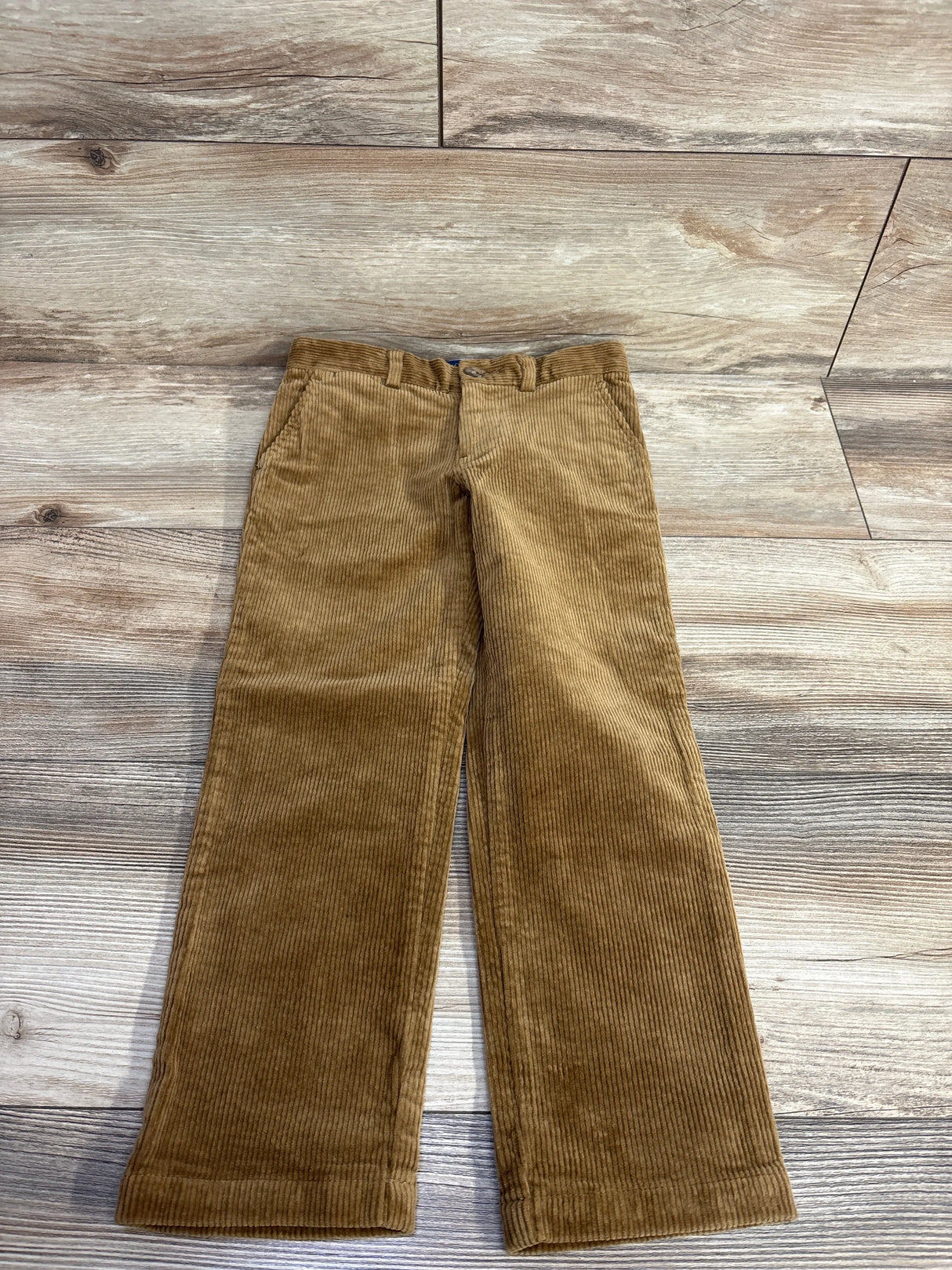 Brown corduroy kids pants with pockets, laid flat on wooden floor