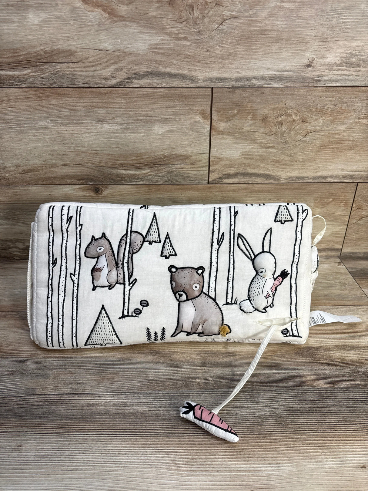 Front view of Crate & Kids tummy time pillow with woodland animals print and attached carrot toy on wood background
