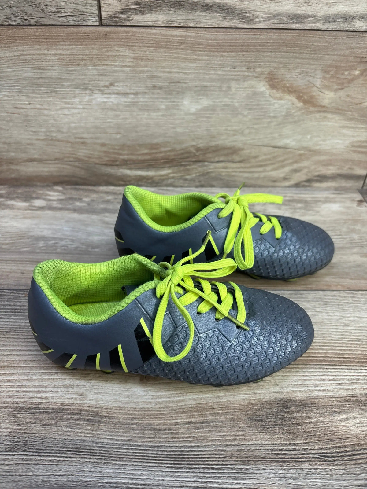 Side view of Hawkwell toddler soccer cleats showcasing gray textured upper and neon yellow laces and lining on wood floor
