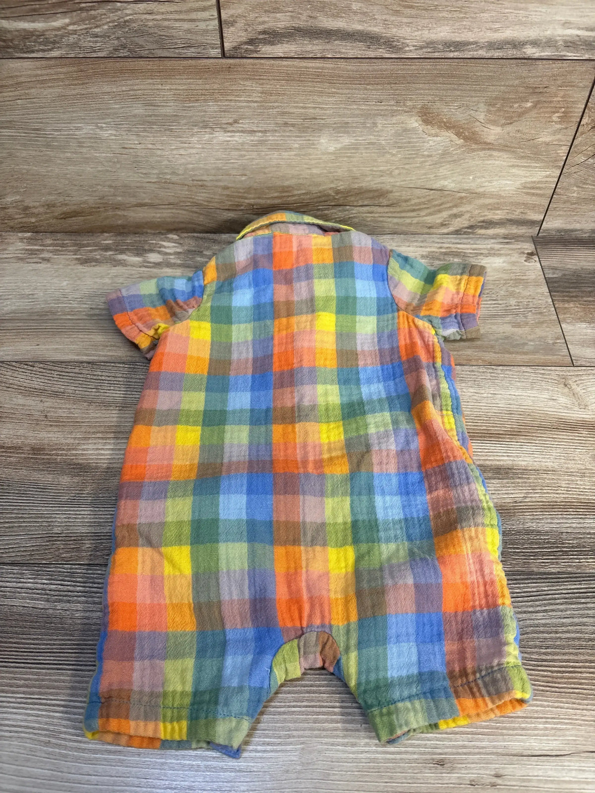 Colorful plaid baby romper with short sleeves, laid flat on wood floor