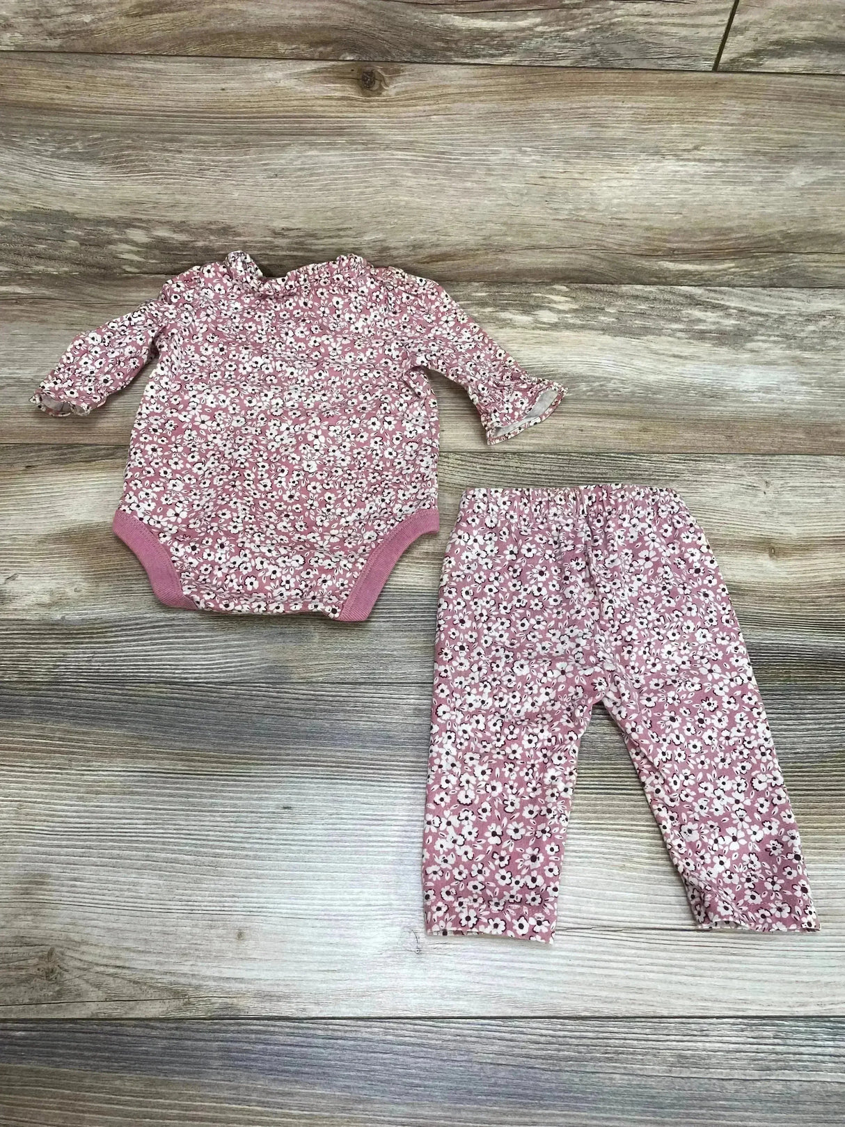 Flat lay of Baby Gap pink floral bodysuit and pants with ruffle collar, snap crotch, and elastic waist on light wood surface