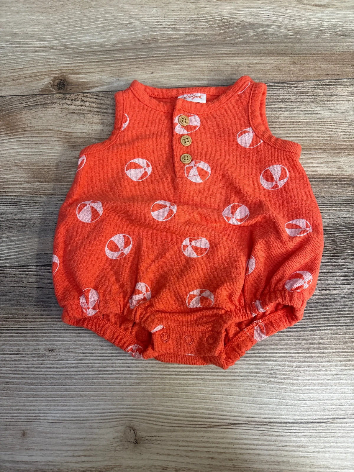 Top-down of Cat & Jack newborn orange henley romper with white beach ball print, three buttons, and elastic legs on wood