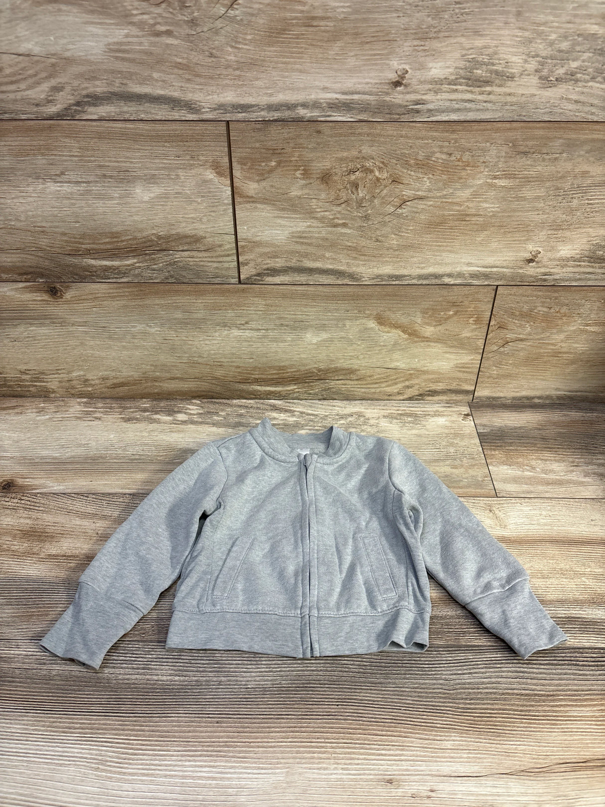 Front view of Hanes grey zip-up toddler sweatshirt showing center zipper, front pockets, and ribbed cuffs on wood background