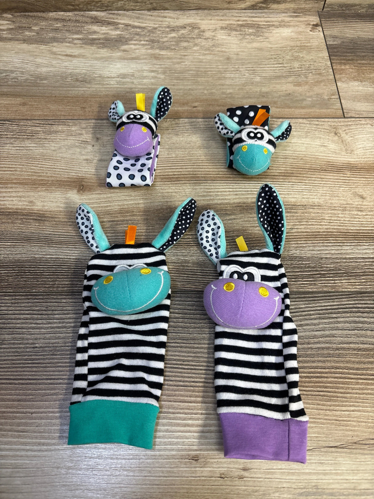 Top-down view of wrist rattles and foot finders showing striped zebra faces in teal and purple on wood background