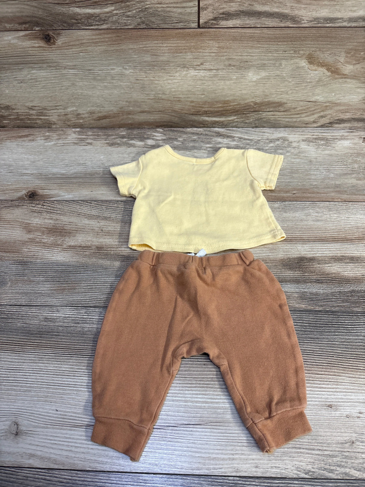 Flat lay of 2-piece Little Explorer set: yellow short-sleeve shirt and brown cuffed pants on wood background