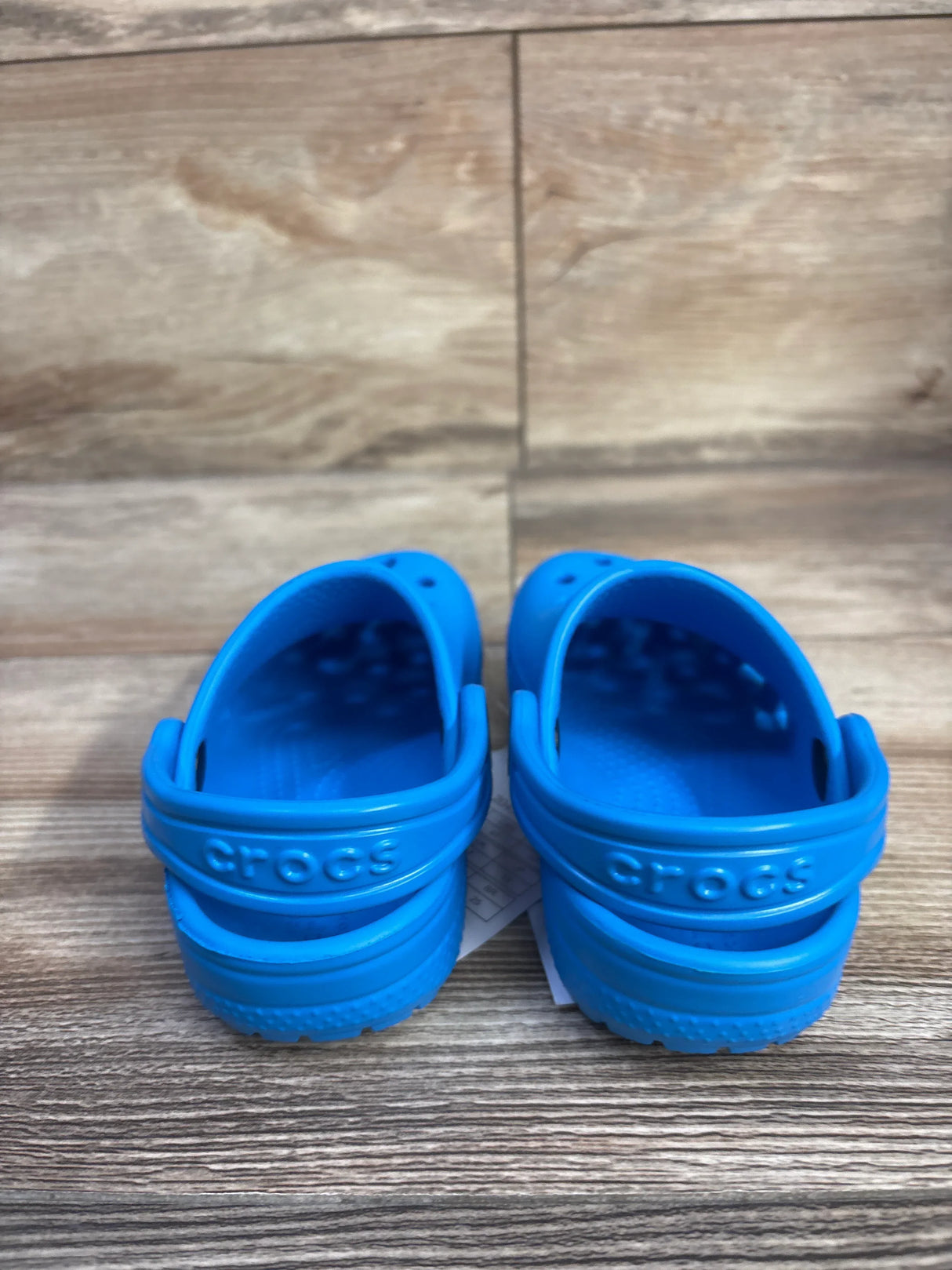 Rear view of toddler blue Crocs Classic Clogs size 7C showing adjustable heel straps with embossed Crocs logo on wood floor