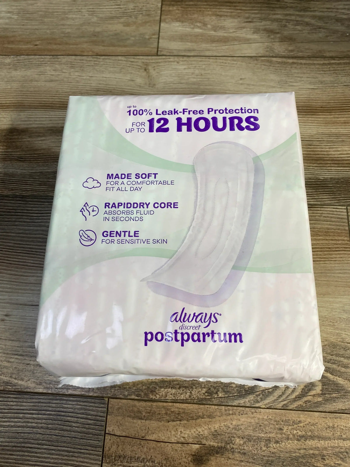 Front view of Always Discreet postpartum pads pack showing '12 HOURS' leak-free protection text, features, on wood floor