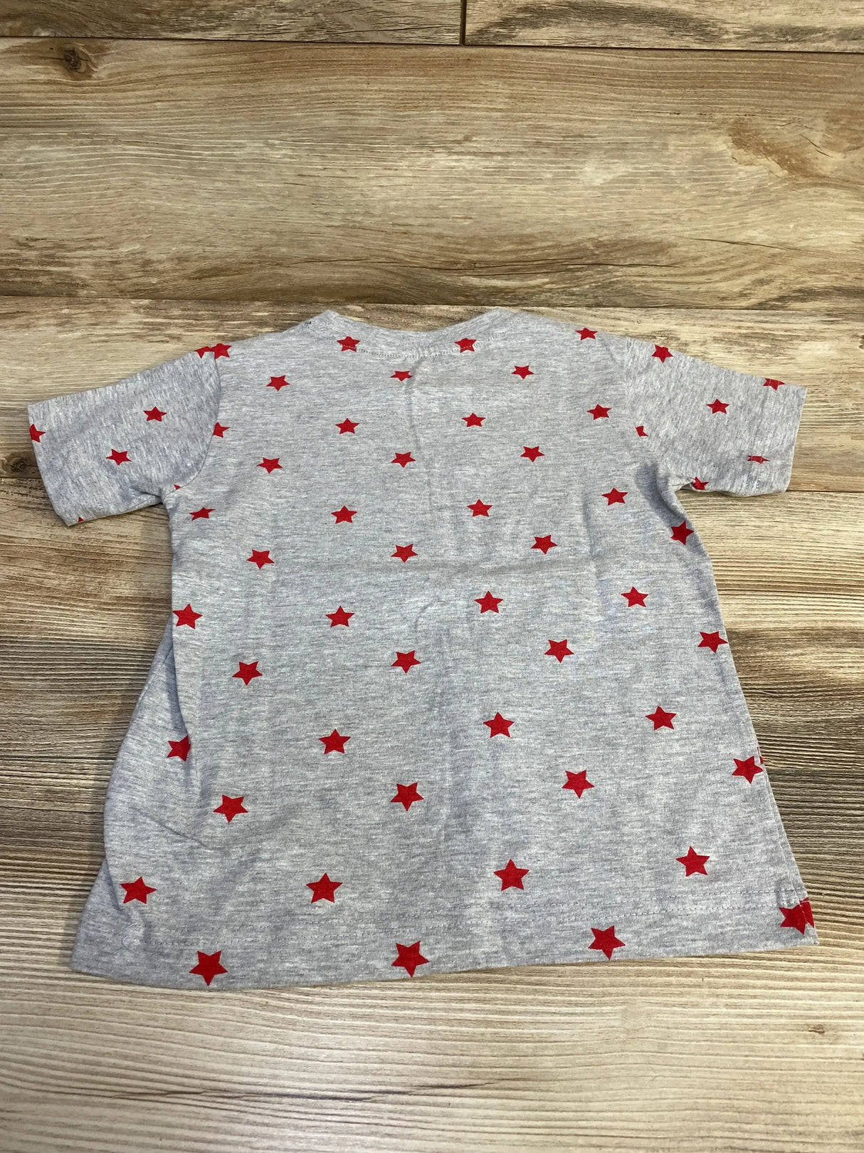 Flat lay of grey toddler T-shirt (4T) showing all-over red star print on wood floor background