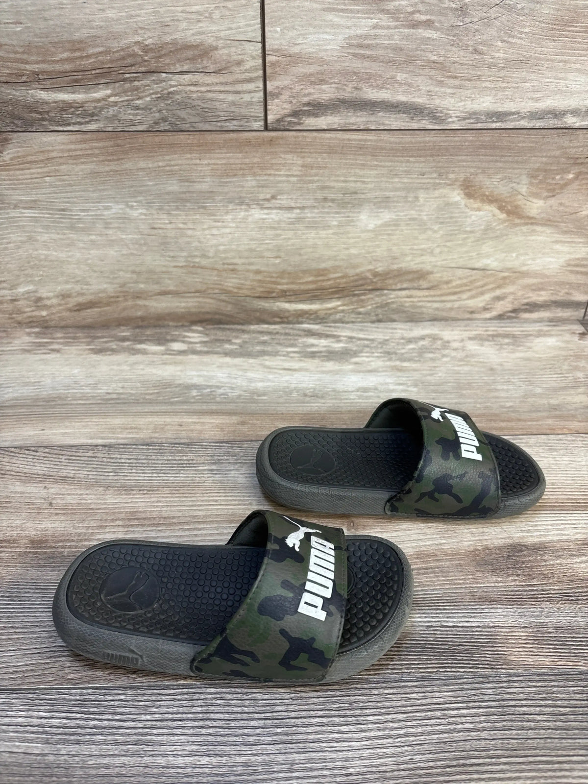 Kids black and camo Puma slide sandals on wood floor