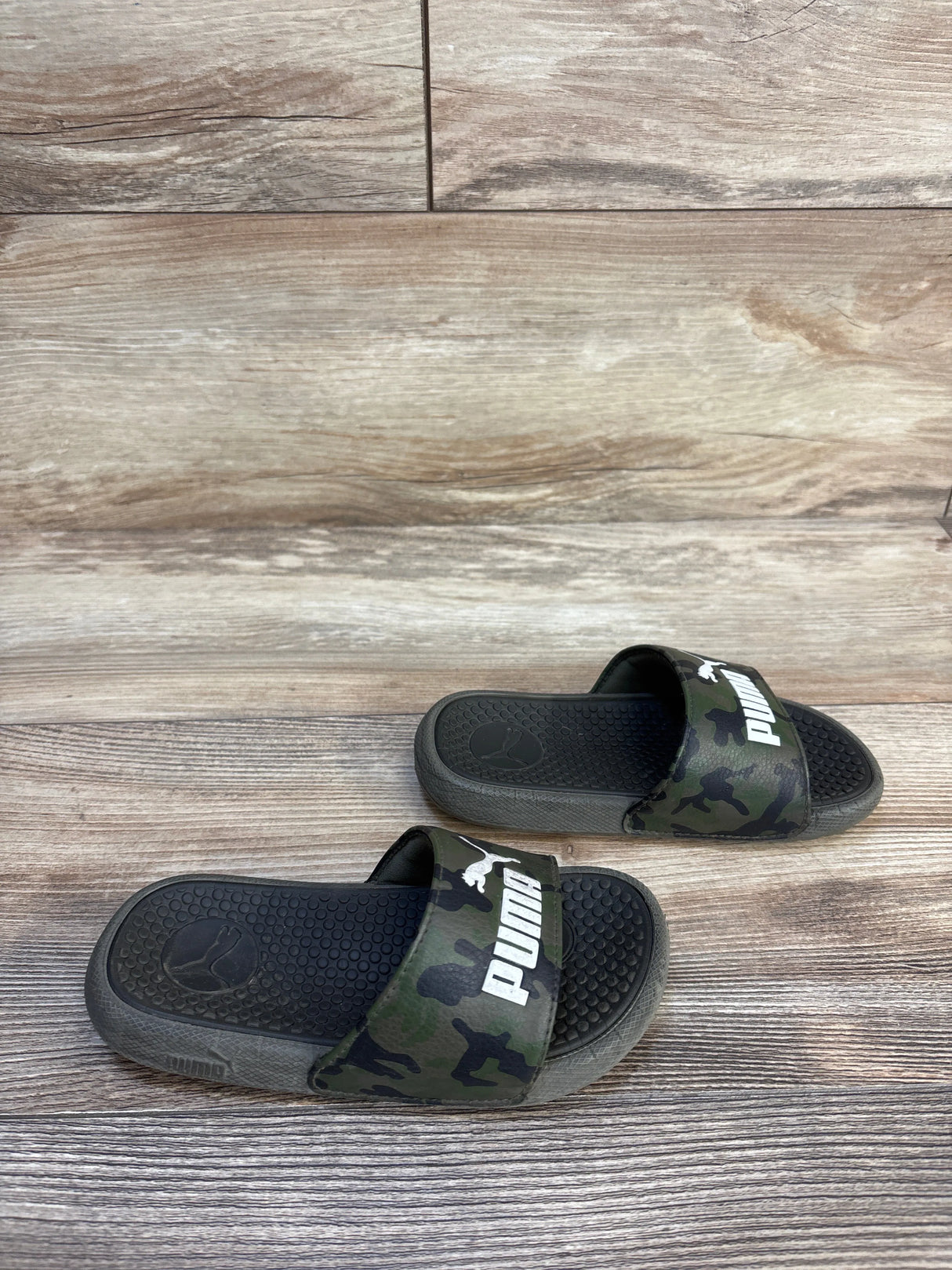 Kids black and camo Puma slide sandals on wood floor