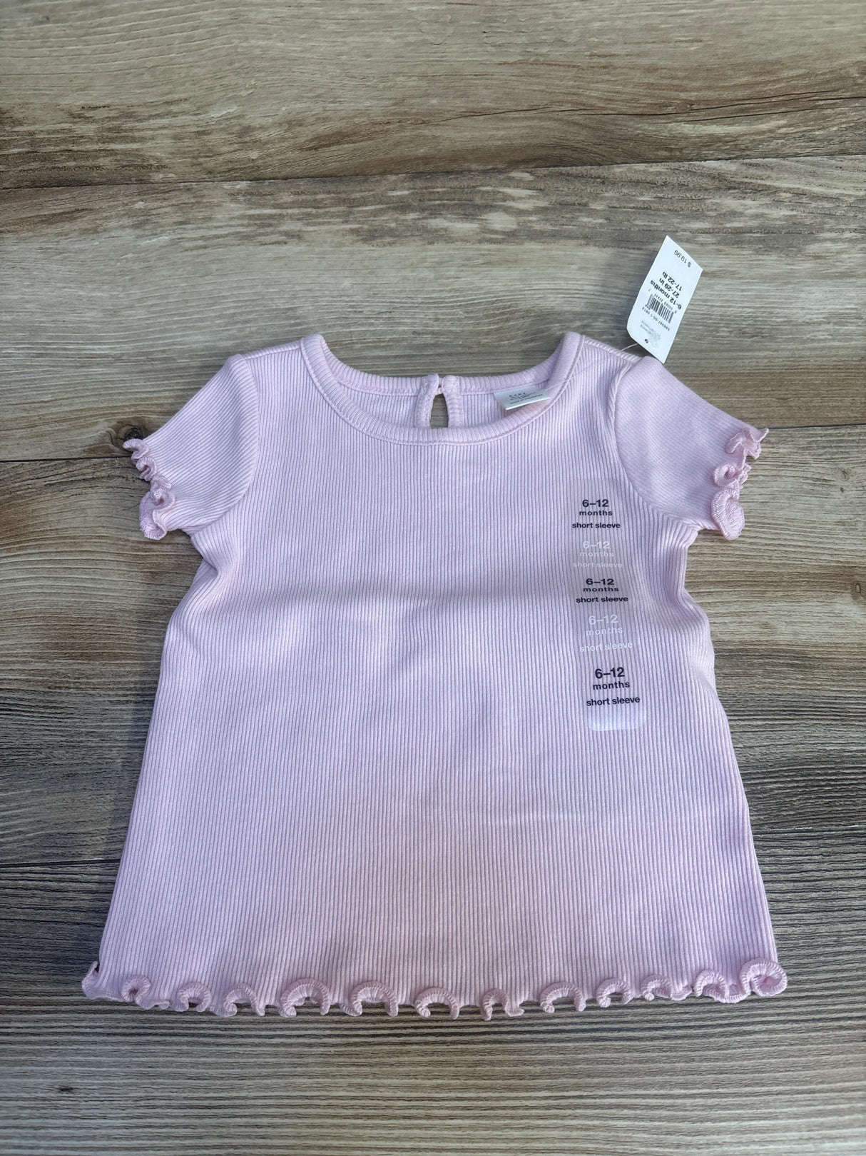 Light pink baby short sleeve shirt with ruffled hems, size 6-12 months, on wood background