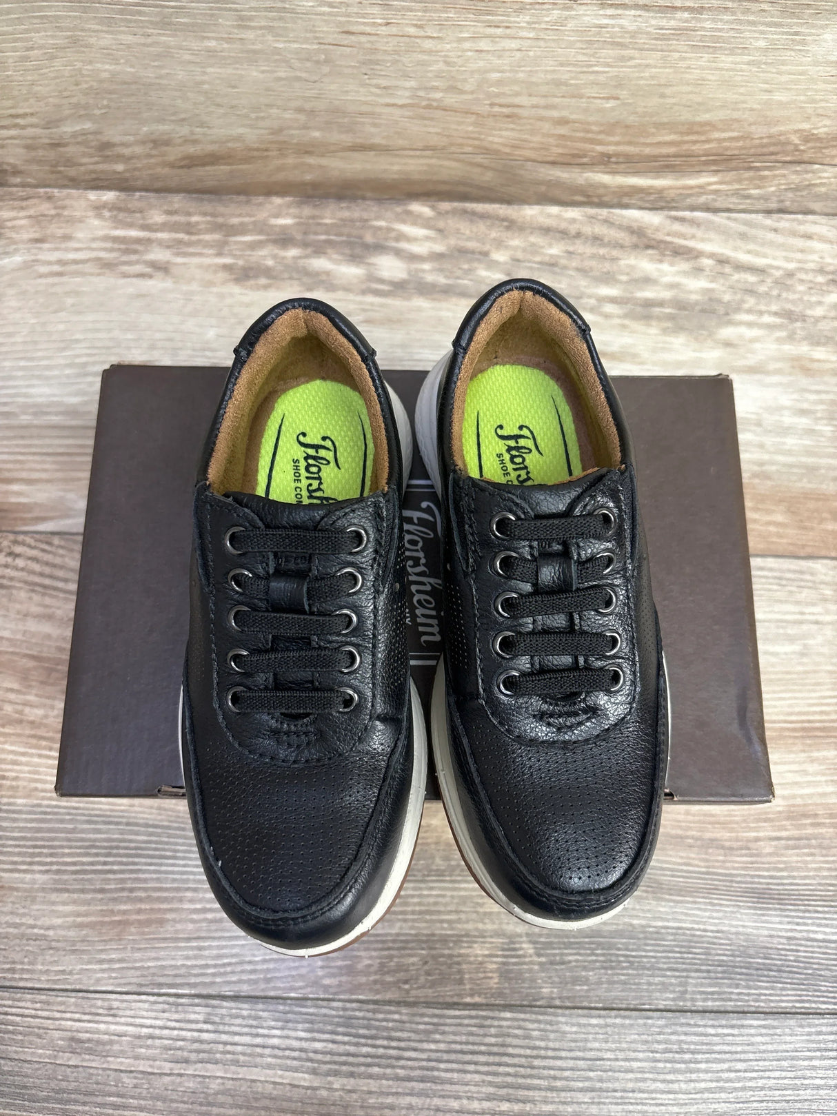 Black leather kids sneakers with white soles on a box, wooden background
