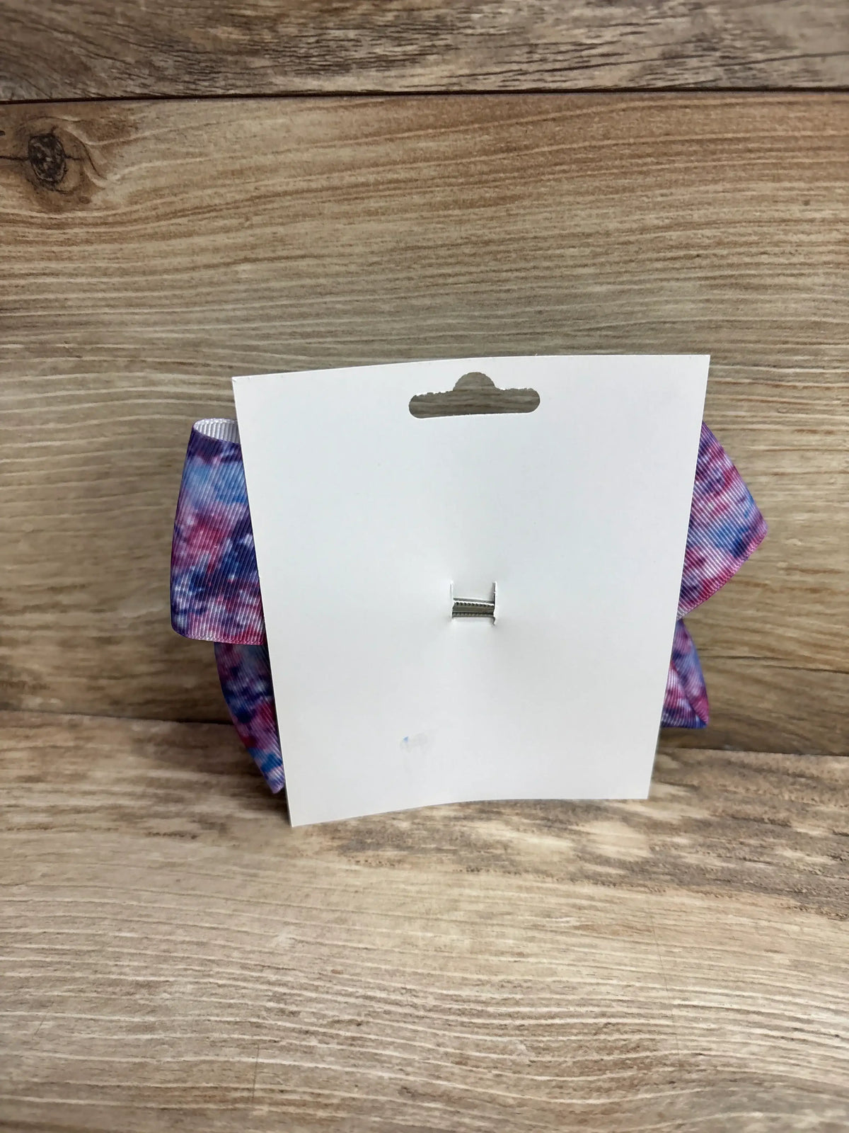 Rear view of large galaxy purple hair bow with tie-dye pattern and silver alligator clip on white card and wood background