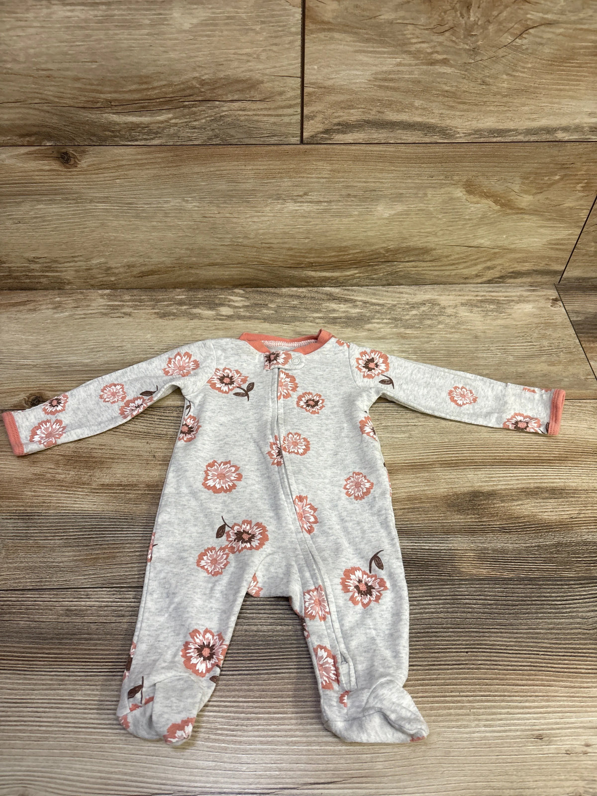Front view of Carter’s grey newborn sleeper showcasing floral print, footed legs, and front zipper on a wood-look floor