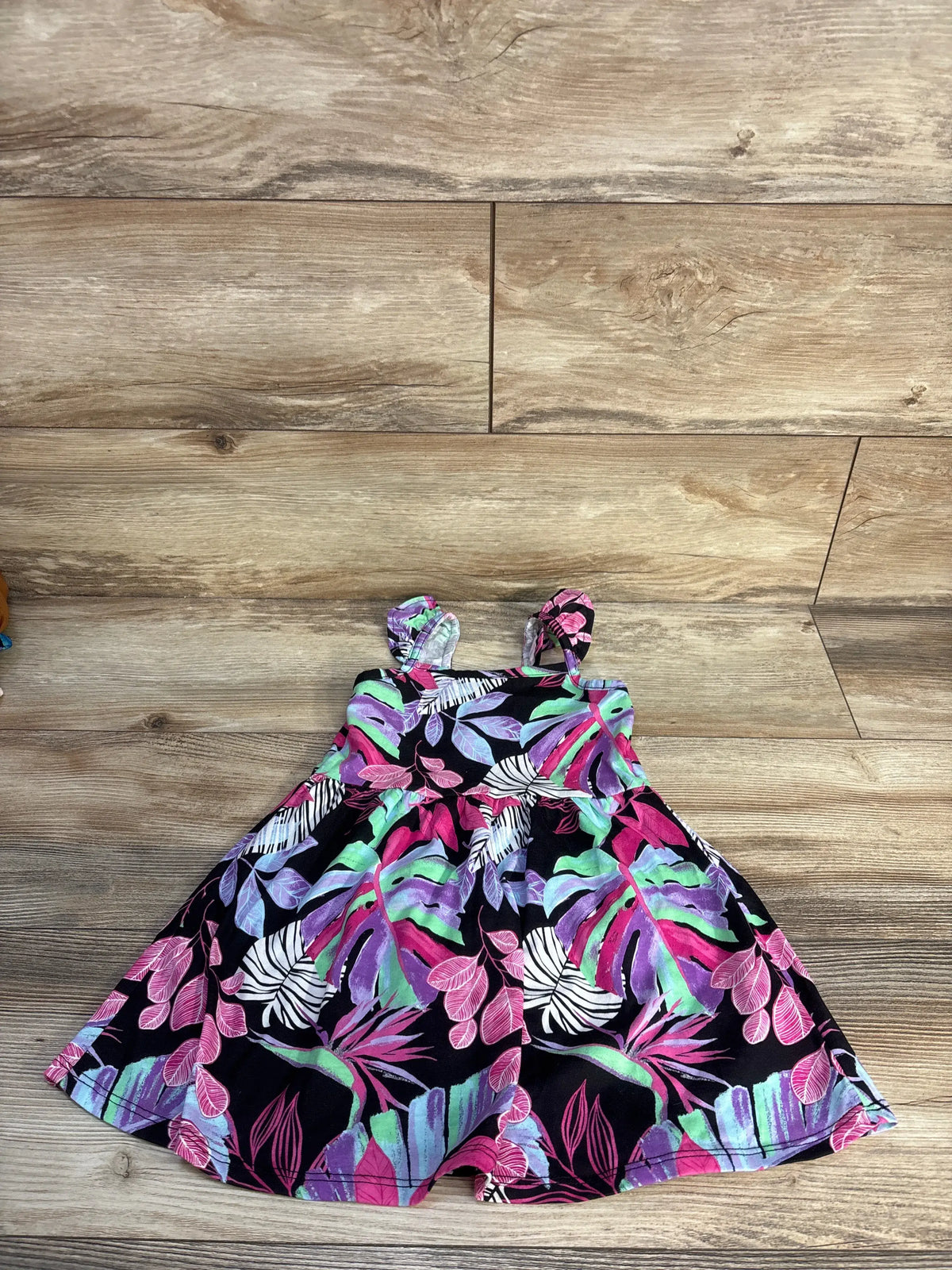 Front view of Children’s Place floral dress in black, size 2T, showcasing colorful floral pattern and gathered waist on wood floor