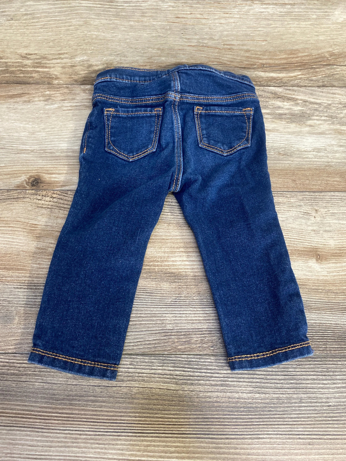 Back view of Old Navy toddler skinny jeans in dark blue showing elastic waistband and rear pockets on a light wood background