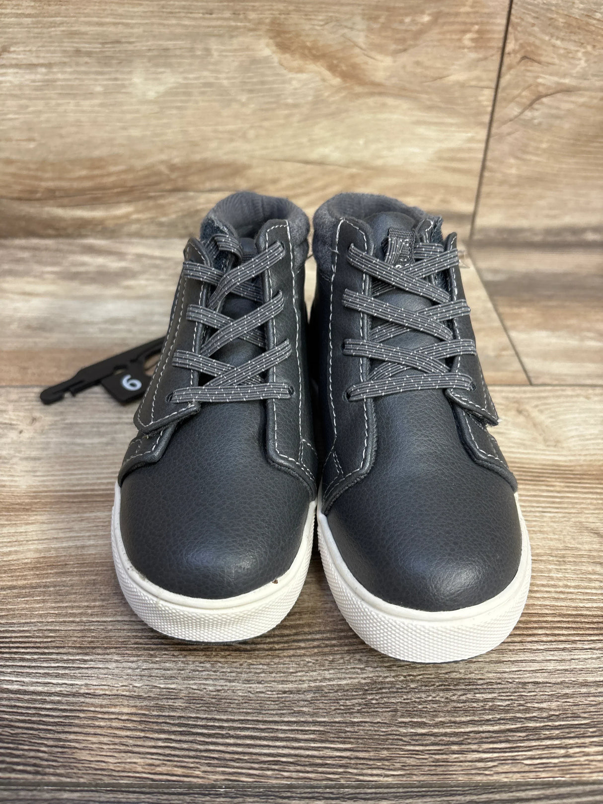 Pair of black kids' high-top sneakers with white soles and grey laces on wood floor