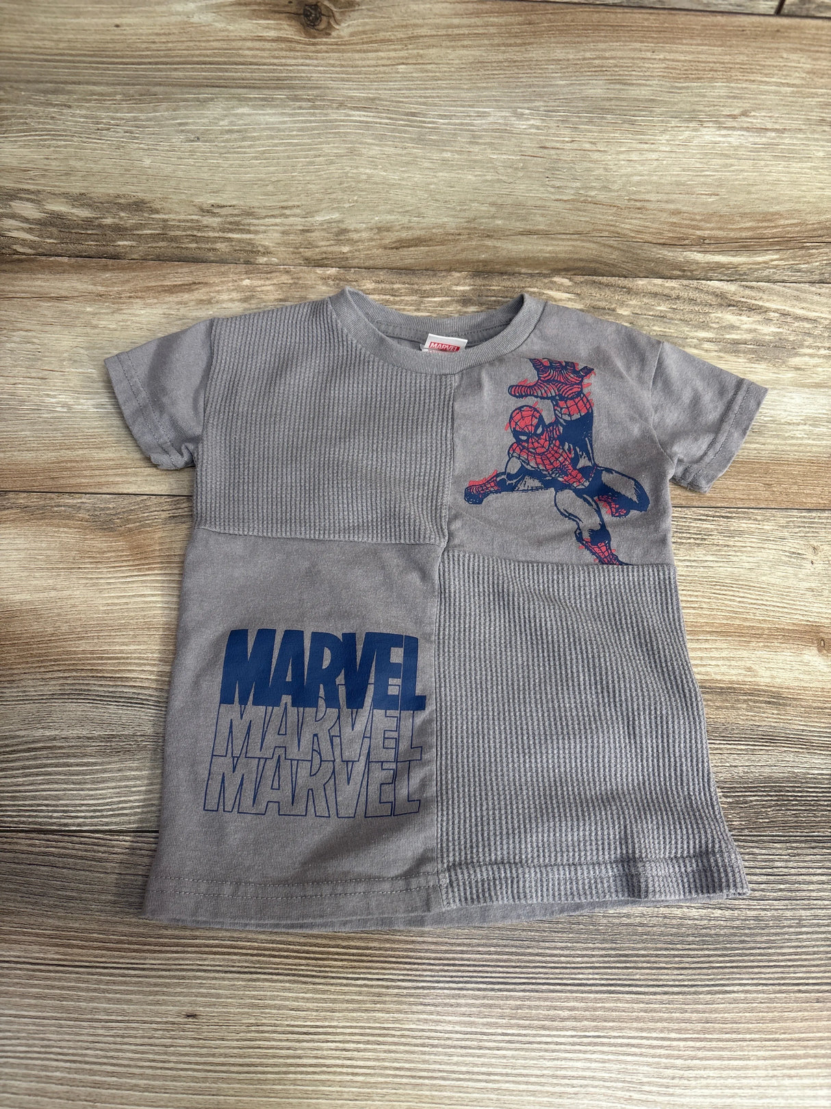 Gray kids Marvel t-shirt featuring Spider-Man graphic and repeated Marvel logo on wooden background