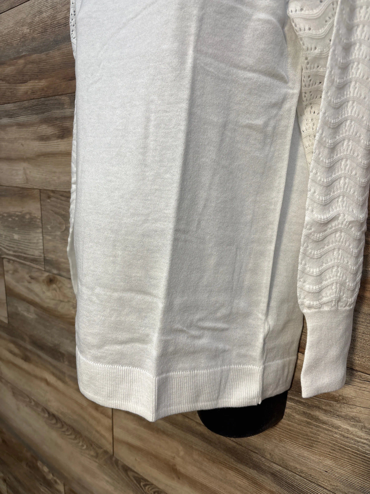 White knit sweater with textured sleeves on wood background
