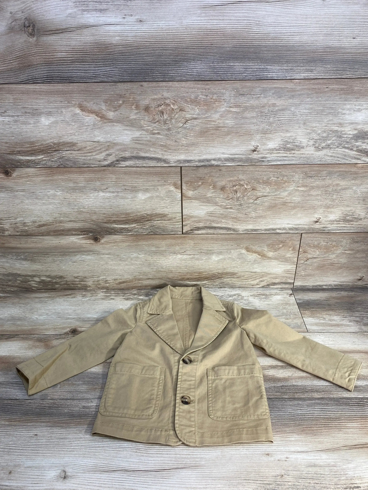Beige toddler blazer jacket with two buttons and front pockets on rustic wood background