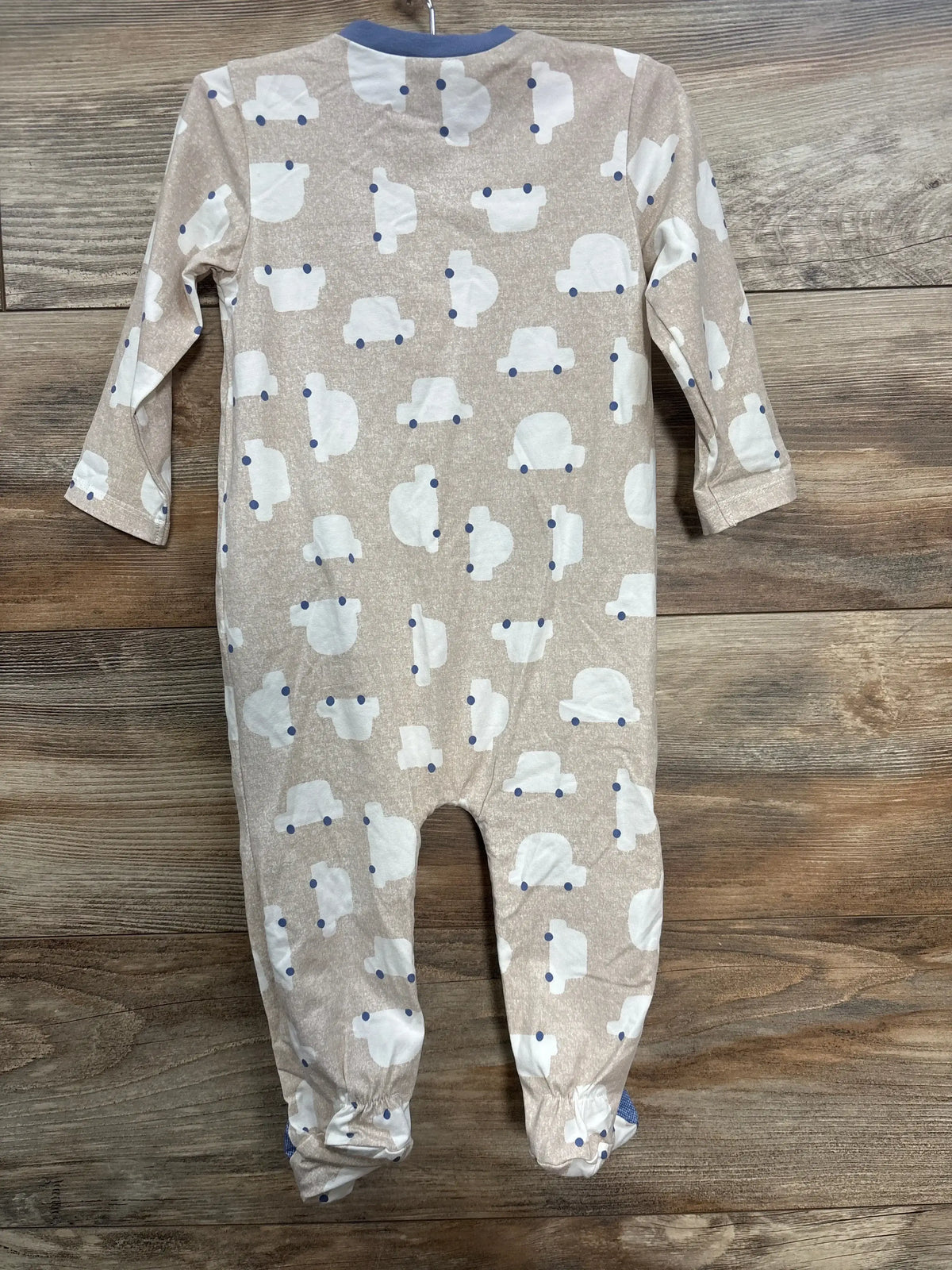 Beige baby onesie with white car prints and blue collar on wooden floor