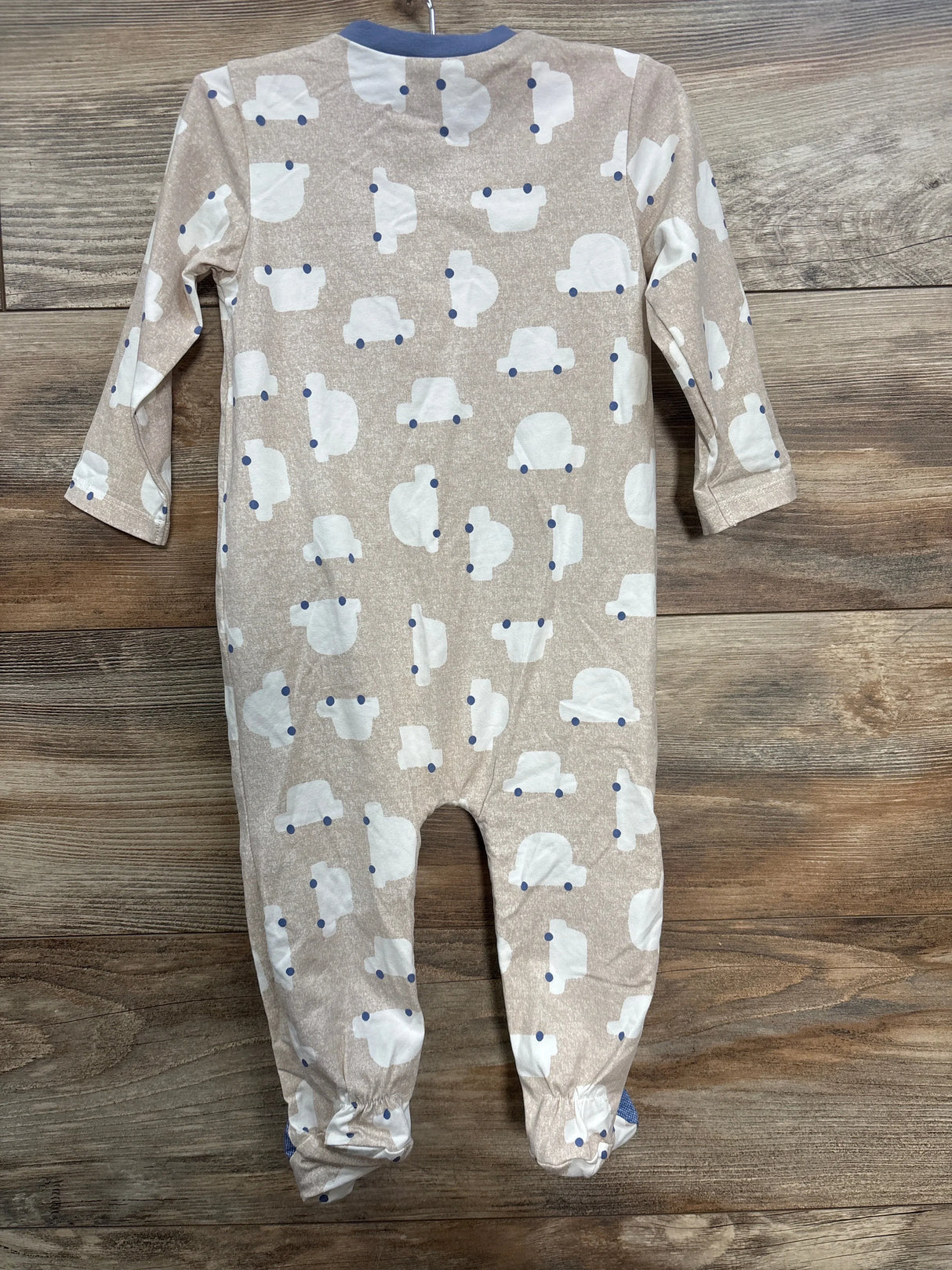 Beige baby onesie with white car prints and blue collar on wooden floor
