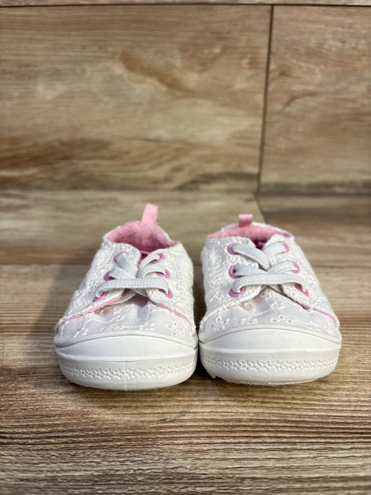 Front view of Wonder Nation baby white eyelet sneakers showcasing bump toe, pink trim and laces on wood floor background