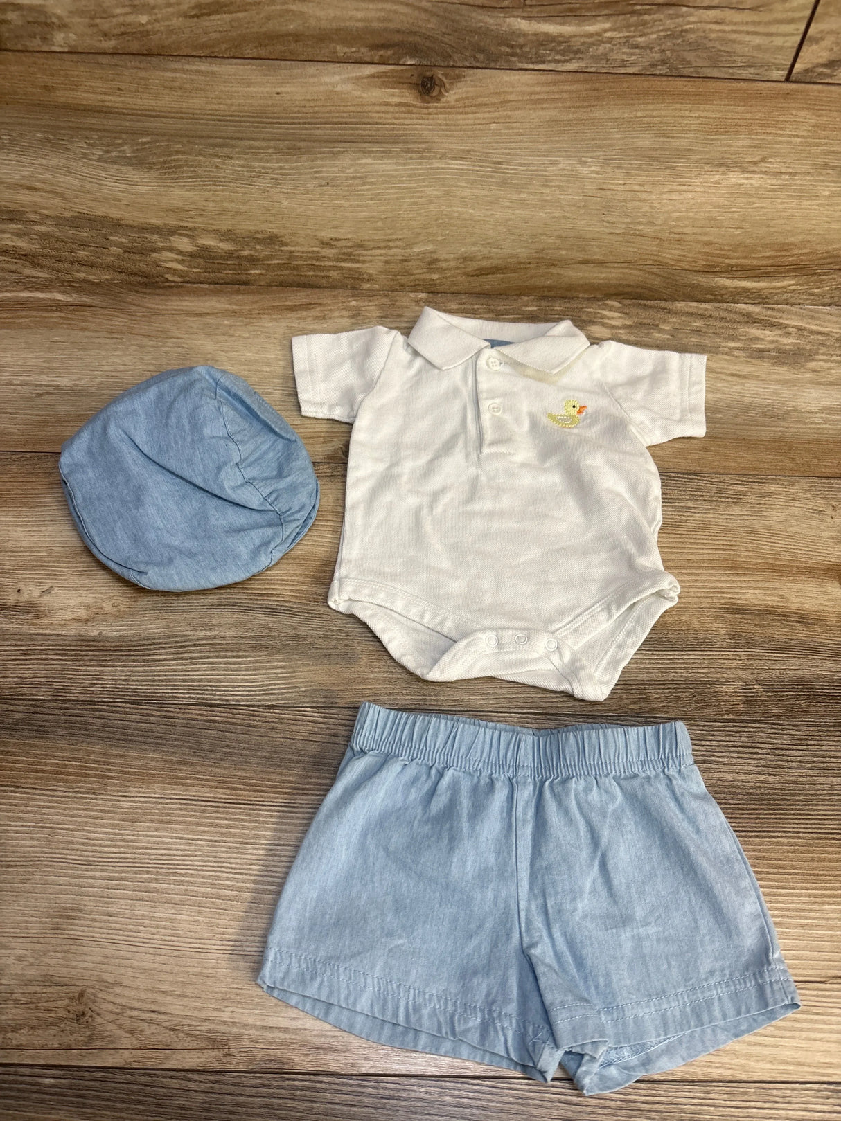 Baby boy outfit with blue shorts, white bodysuit, and matching blue cap on wood background