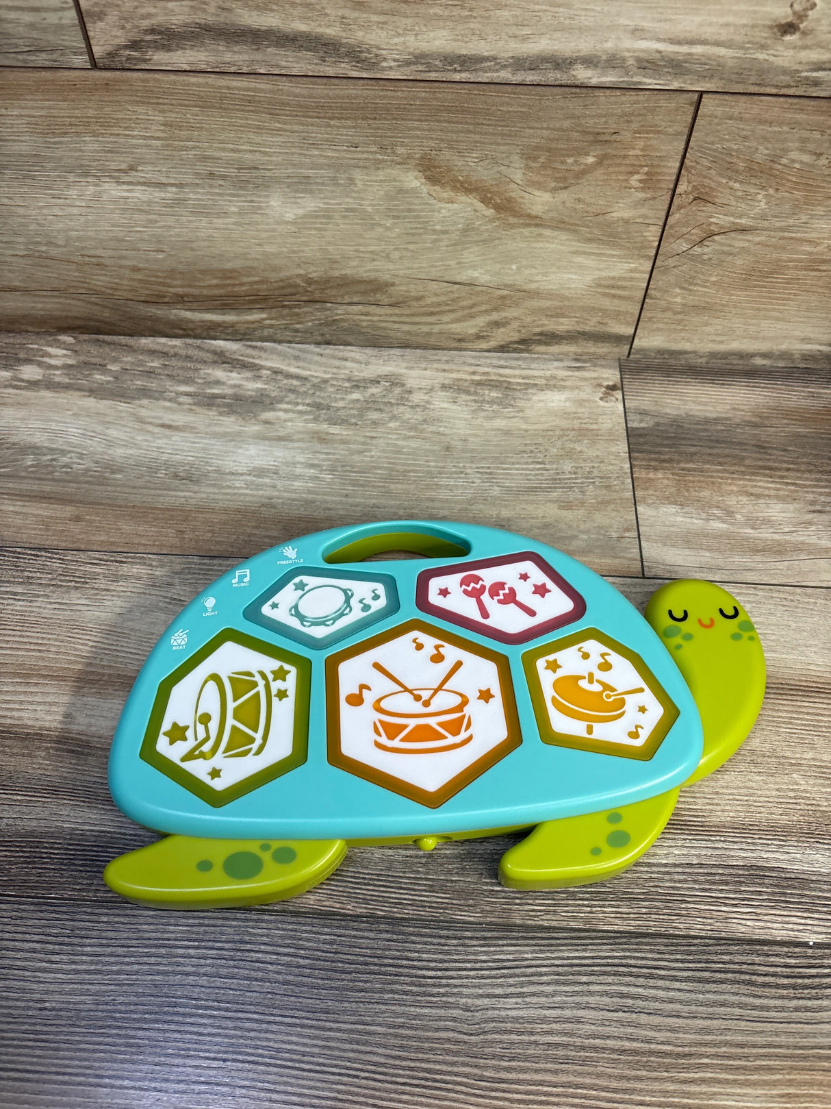 Top-down view of Gigglescape Turtle electronic drum showcasing five light-up hexagon drum pads and smiling turtle handle on wood floor background