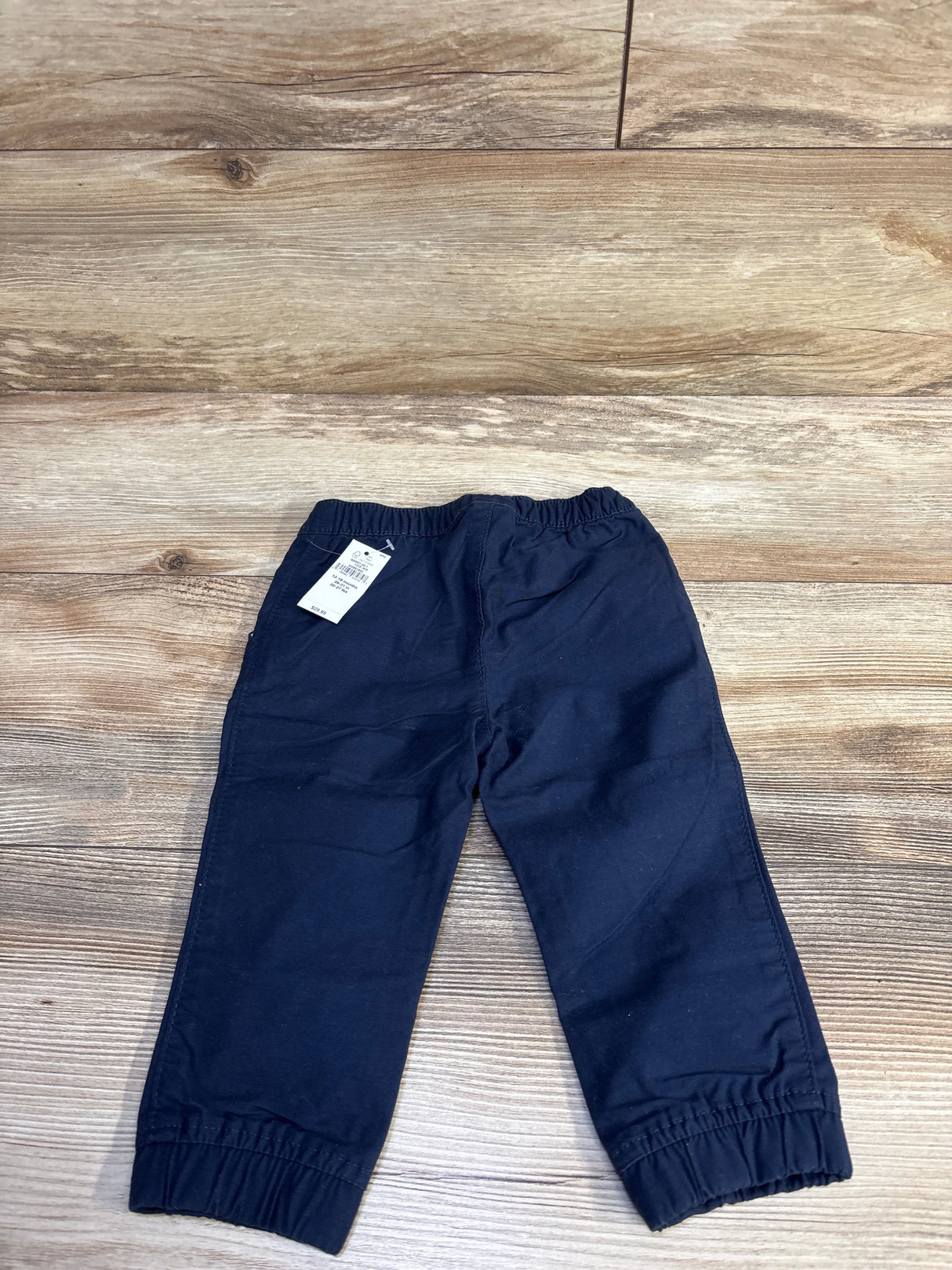 Top-down view of Baby Gap navy joggers showing elastic waistband, drawstring, elastic cuffs and attached tag on wood floor