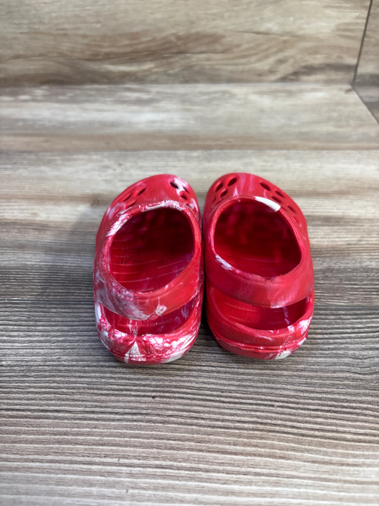 Rear view of Wonder Nation USA tie-dye toddler clogs, red with white marks, scuffed heels on wood-grain surface, size 5C