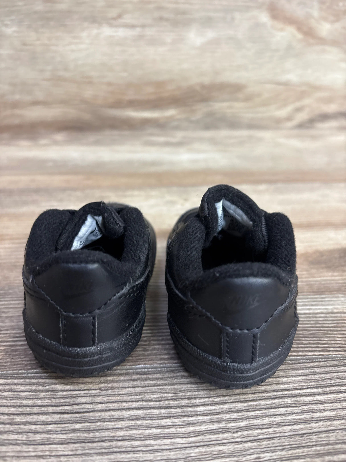 Pair of black Nike toddler shoes on wooden surface, children's footwear for resale
