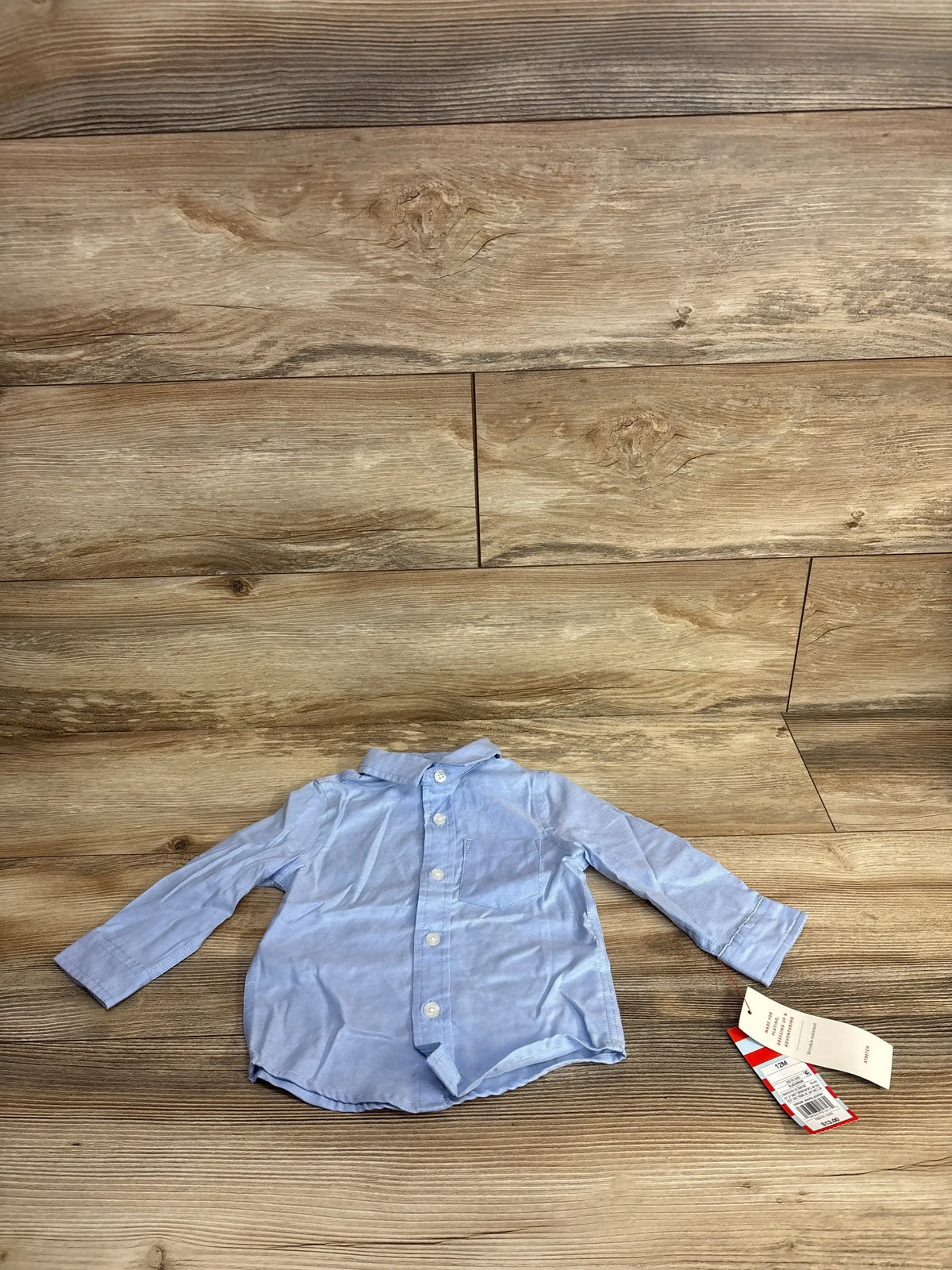 Light blue long sleeve baby shirt with buttons and tags on wooden background
