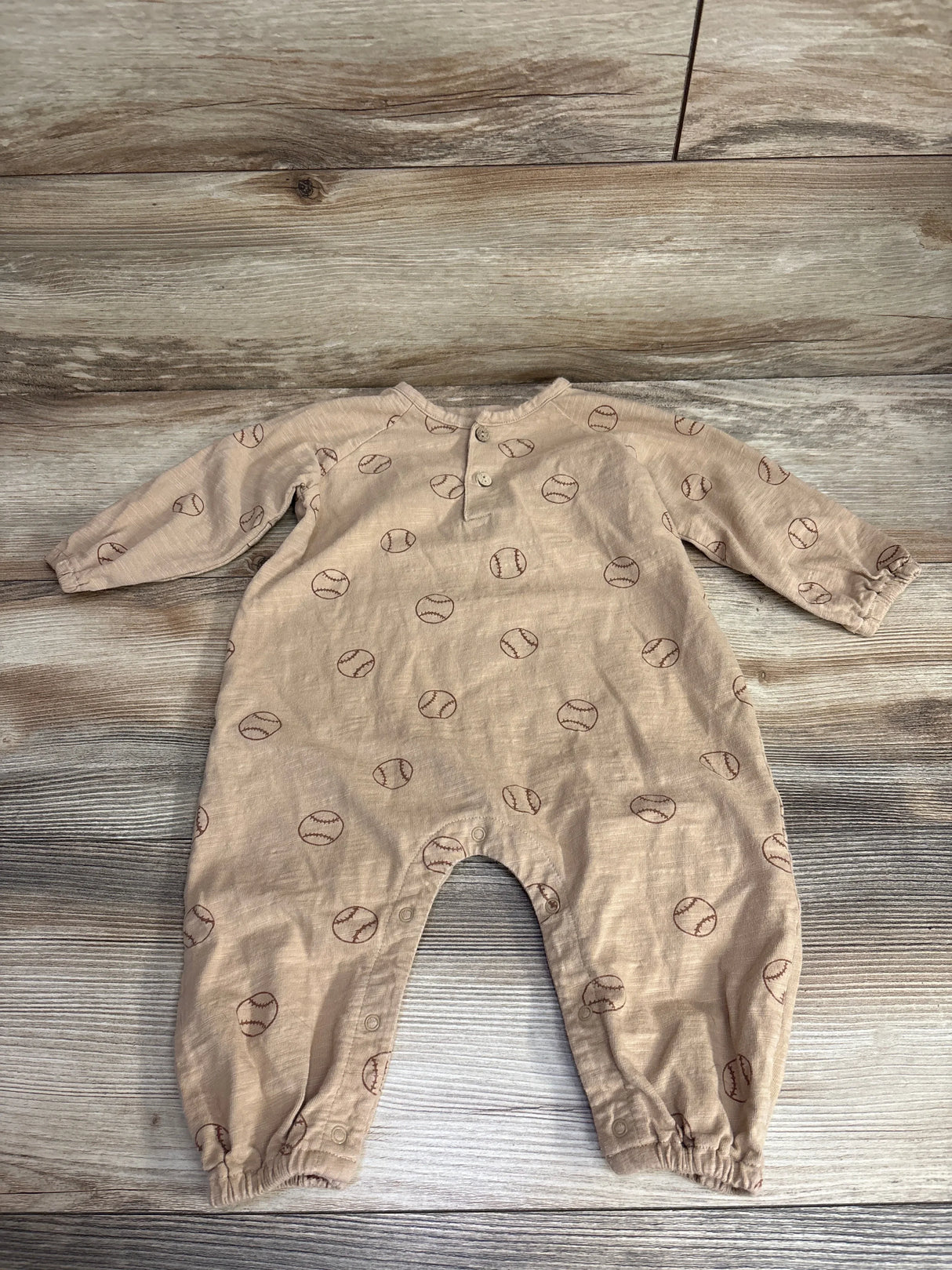 Beige baby romper with long sleeves and brown baseball print, laid flat on wood floor